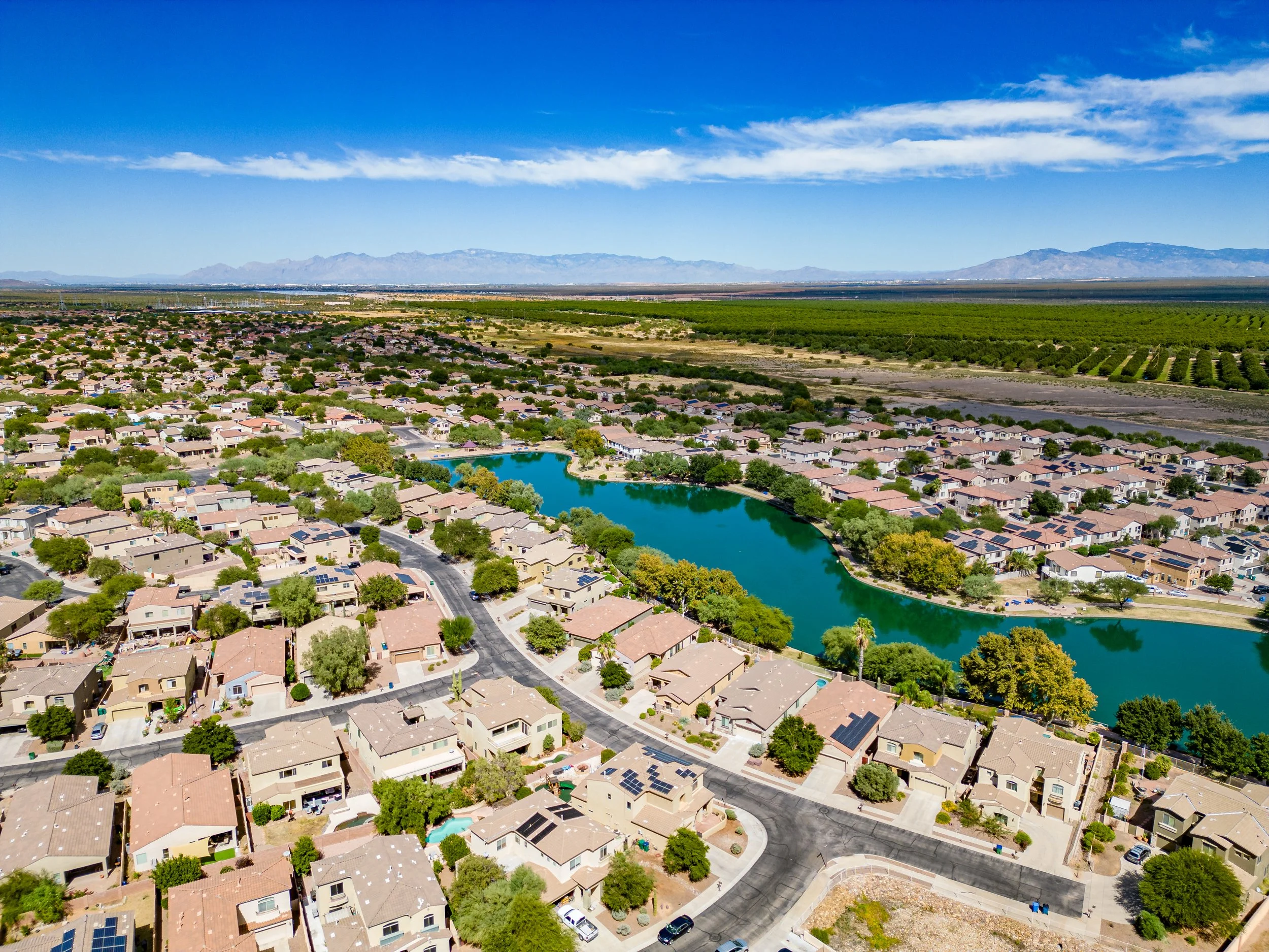 Drone aerial view of Sahuarita Lake and the surrounding residential community in Sahuarita, Arizona, featuring scenic waterfront homes, parks, and mountain views.