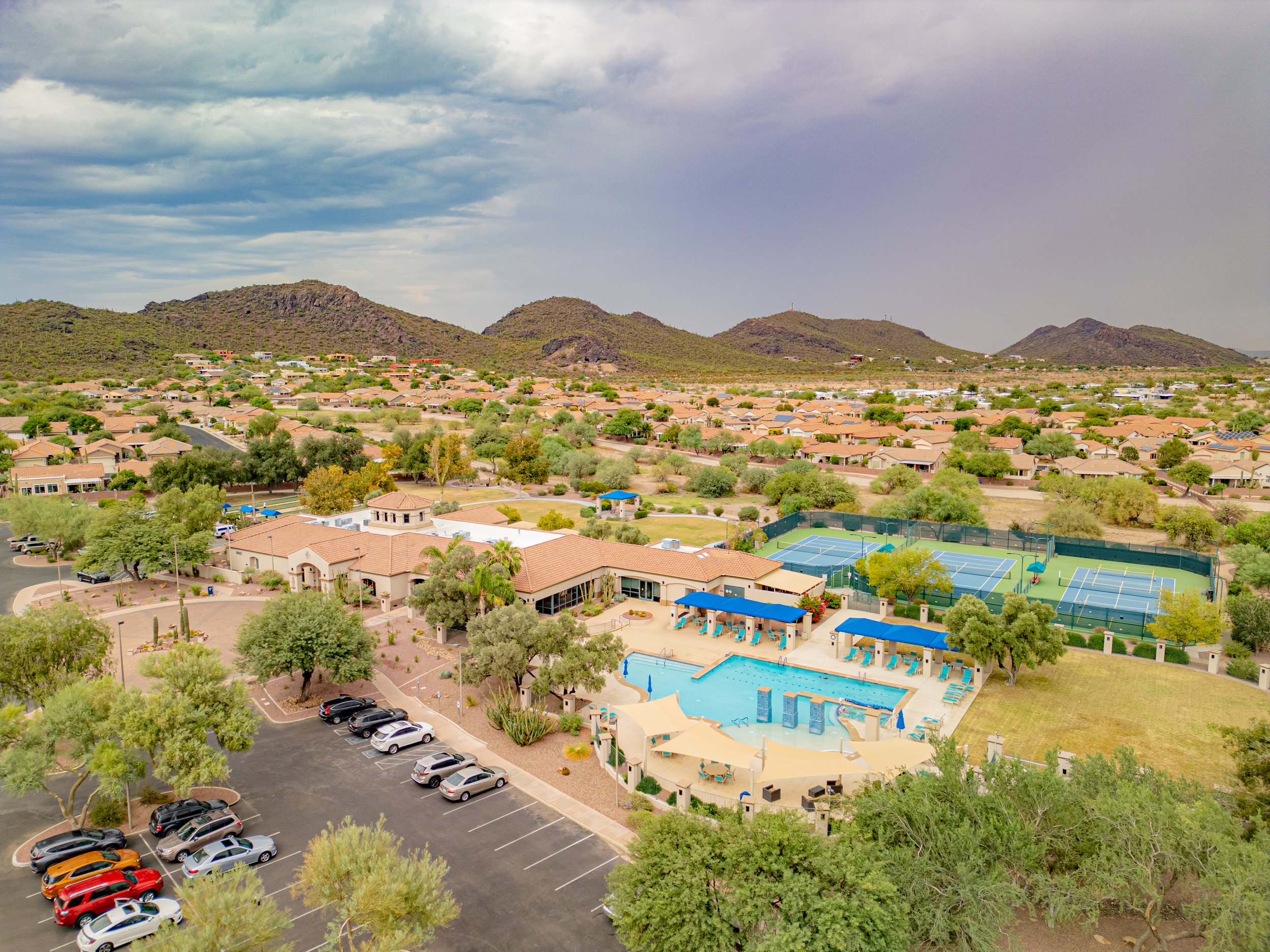 Drone photo of an active adult community in the Continental Ranch area of Marana, Arizona, showing a clubhouse, swimming pool, tennis courts, desert landscaping, and mountain scenery in the background.