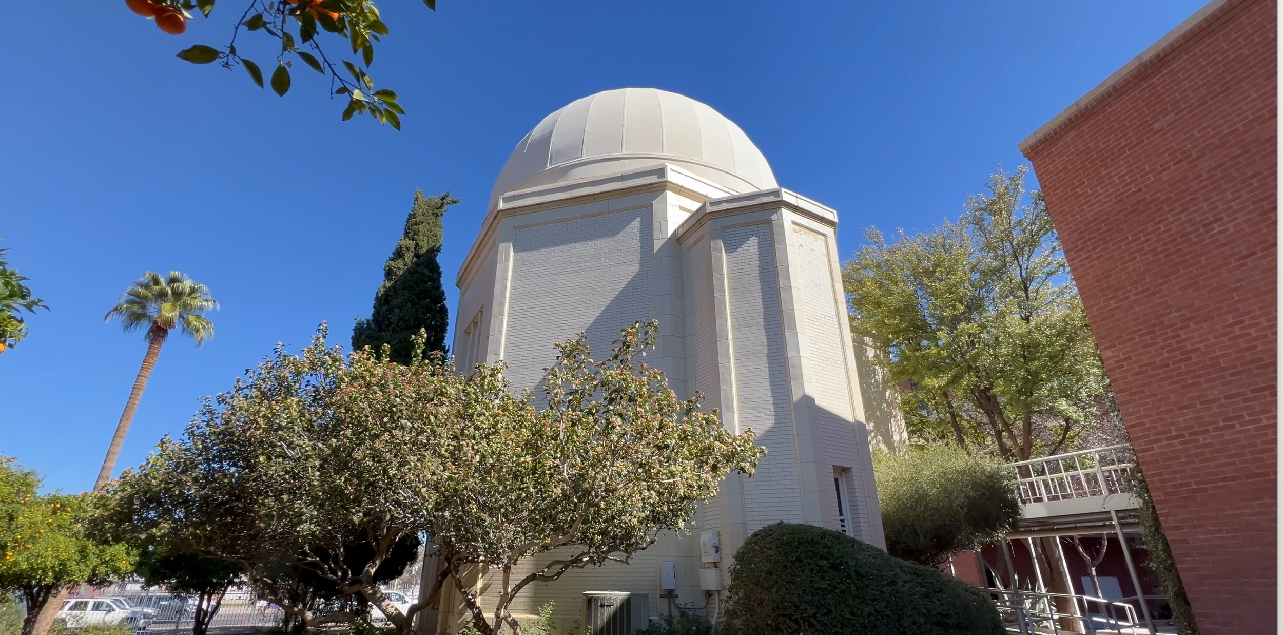 White dome of Steward Observatory at the University of Arizona in Tucson, surrounded by trees under a clear blue sky
