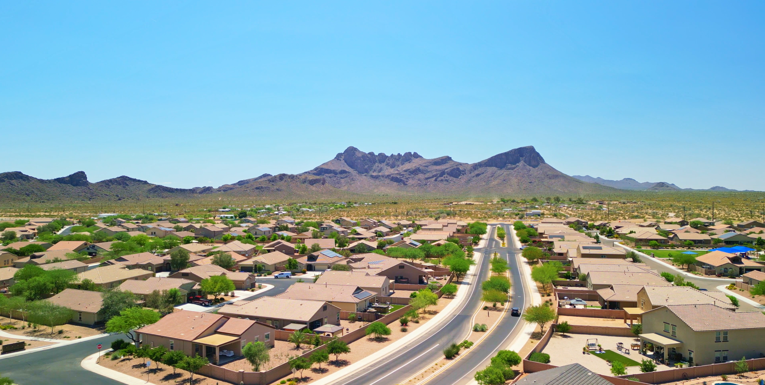 Aerial drone photo of the Saguaro Bloom neighborhood in Marana, Arizona, featuring desert landscaping, suburban homes, and mountain scenery under a clear blue sky.