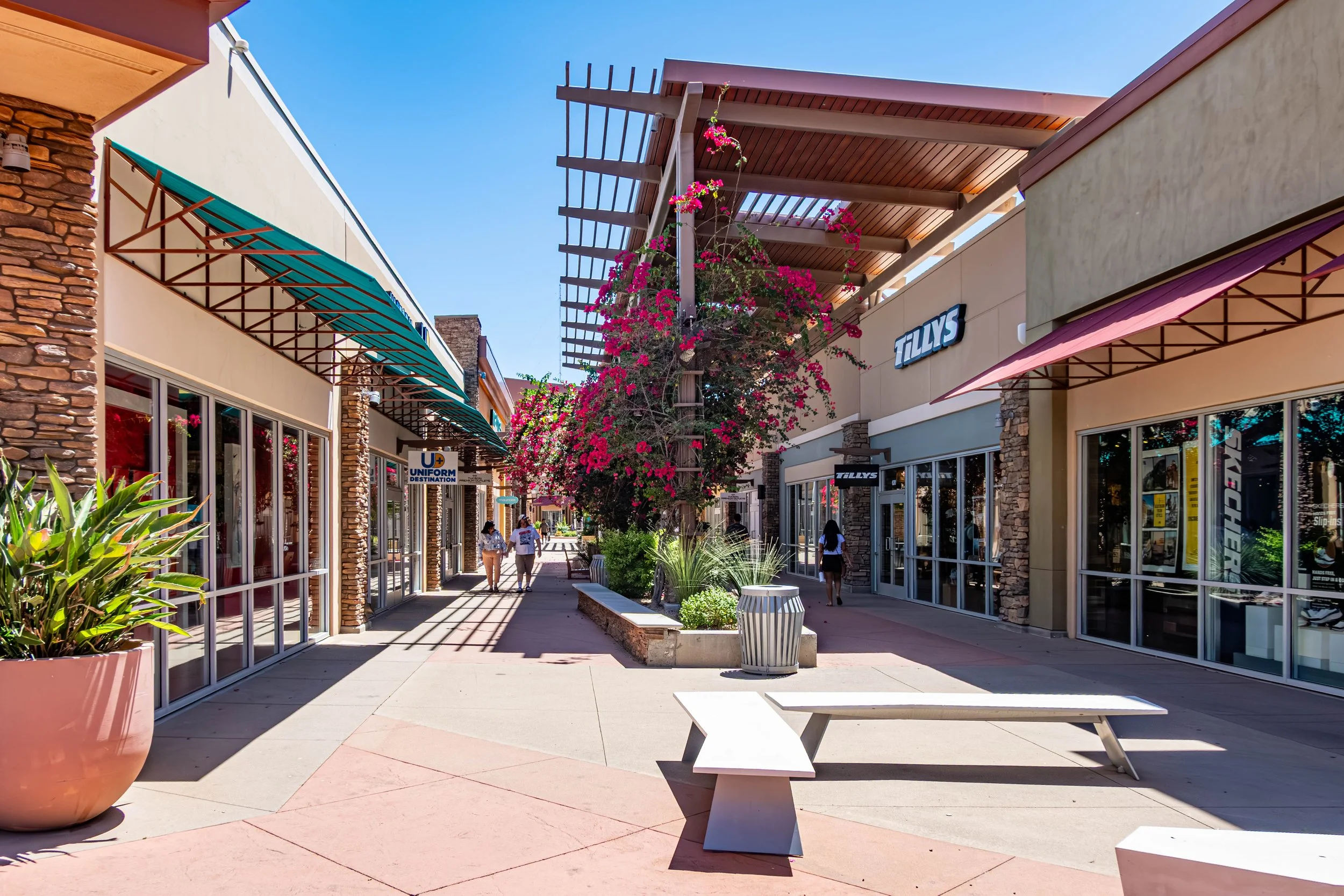 Photo of the Tucson Premium Outlets in Marana, Arizona, featuring outdoor shopping walkways, retail storefronts, desert landscaping, and colorful bougainvillea flowers.