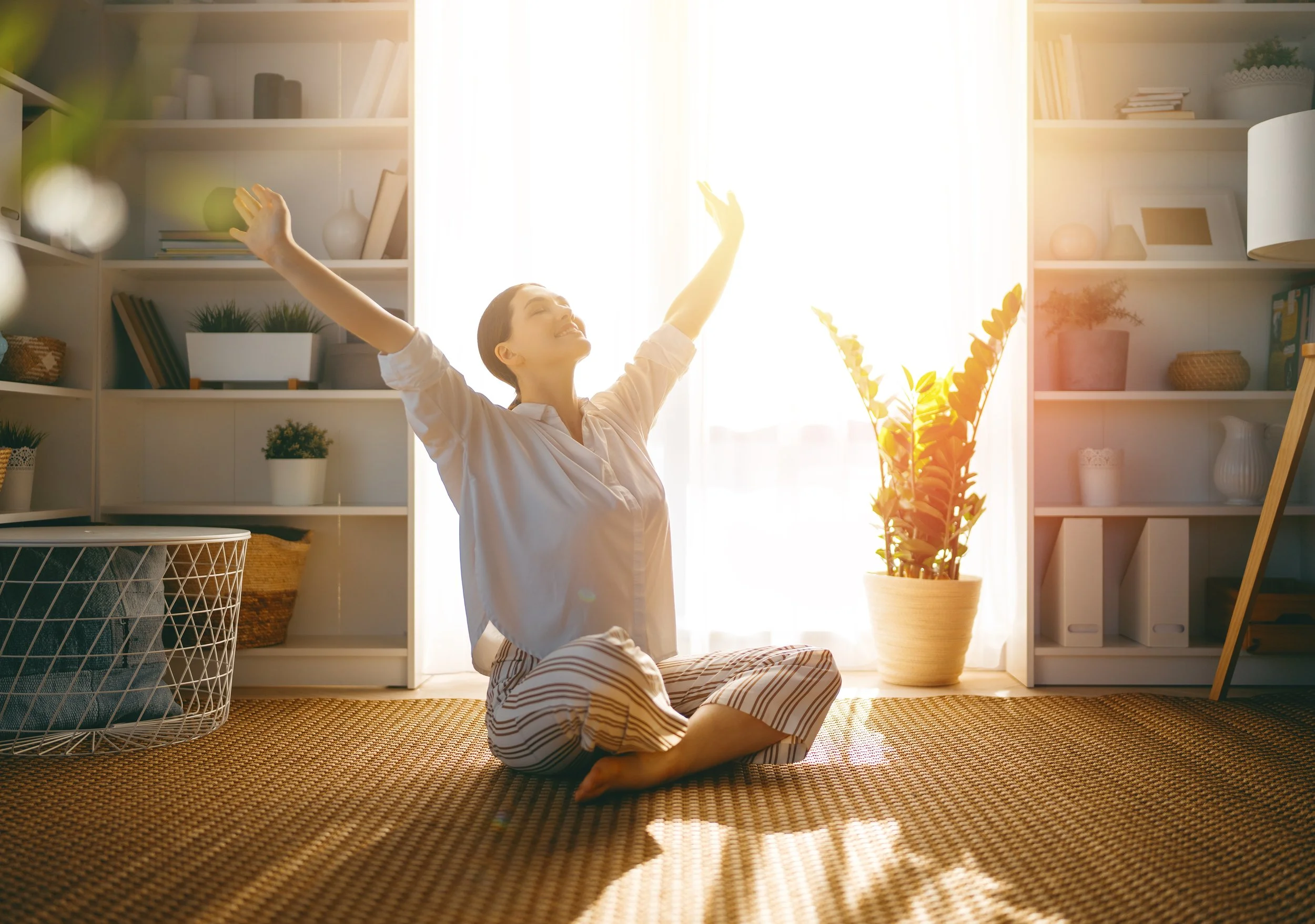 Woman stretching in bright morning sunlight indoors, illustrating circadian rhythm support and improved sleep quality.