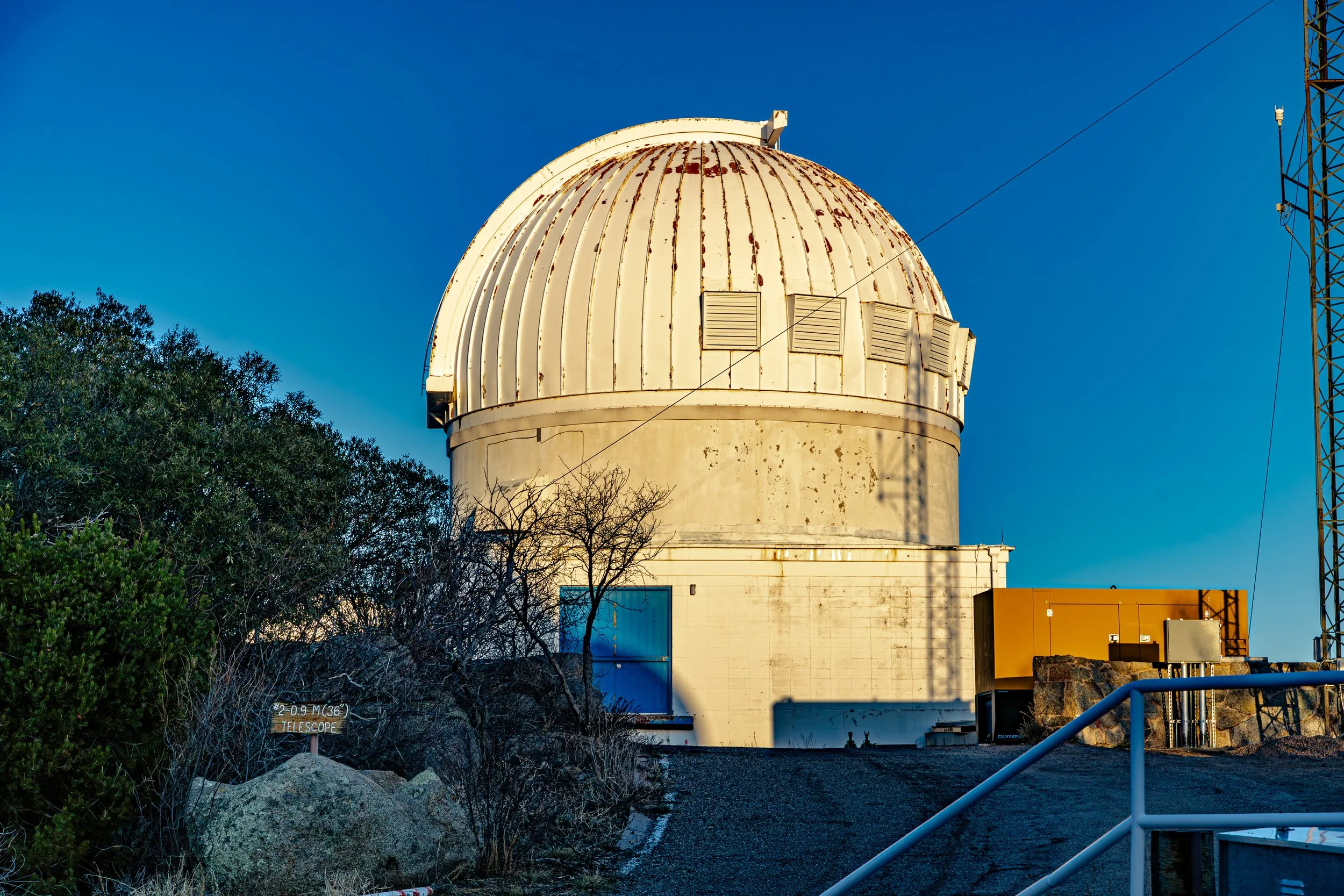 White telescope dome at Kitt Peak National Observatory near Tucson, Arizona, surrounded by mountain vegetation beneath a blue sky.