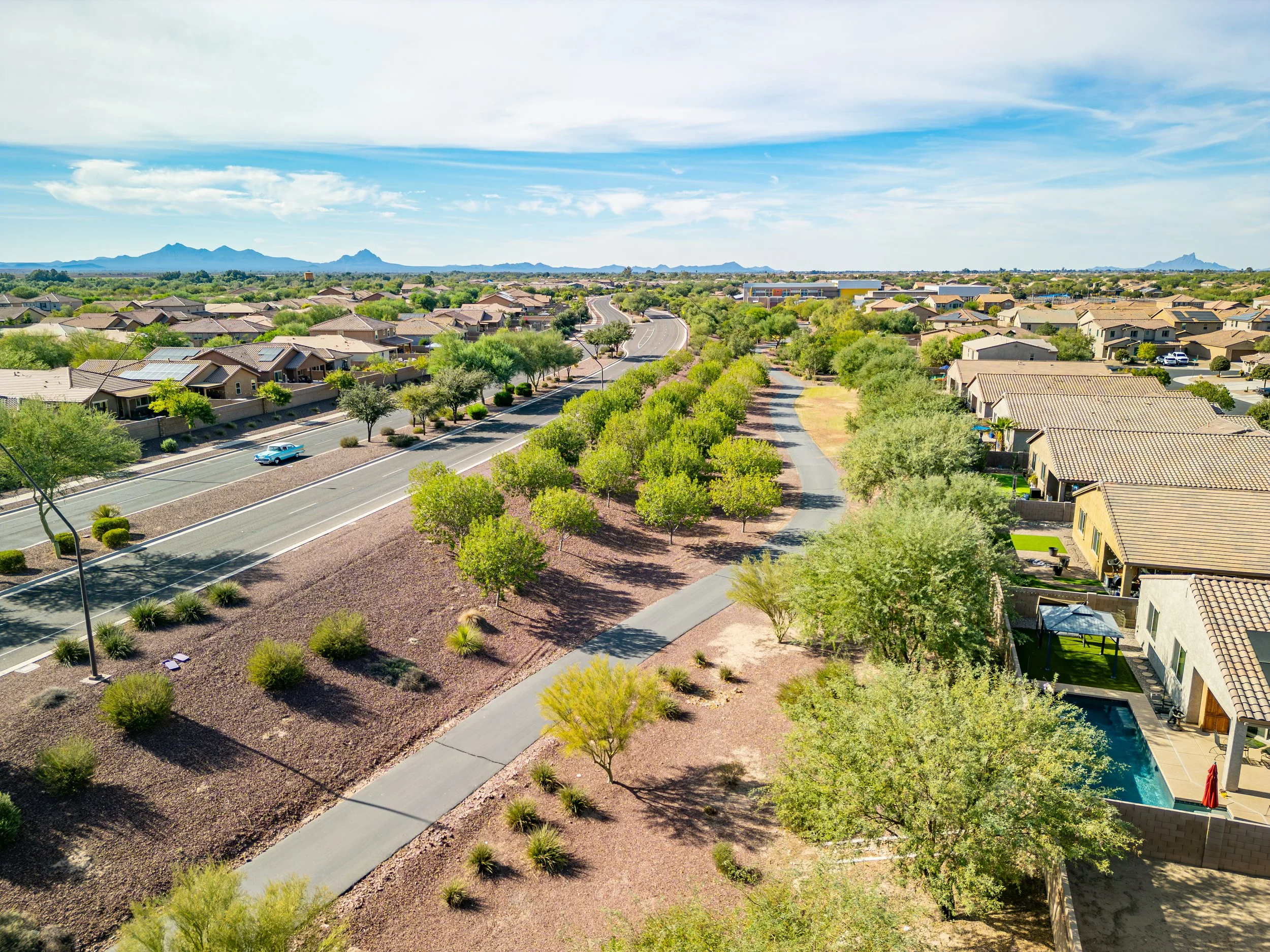 Drone photo overlooking the Gladden Farms neighborhood in Marana, Arizona, with suburban homes, walking trails, desert landscaping, and mountain views under a blue sky.