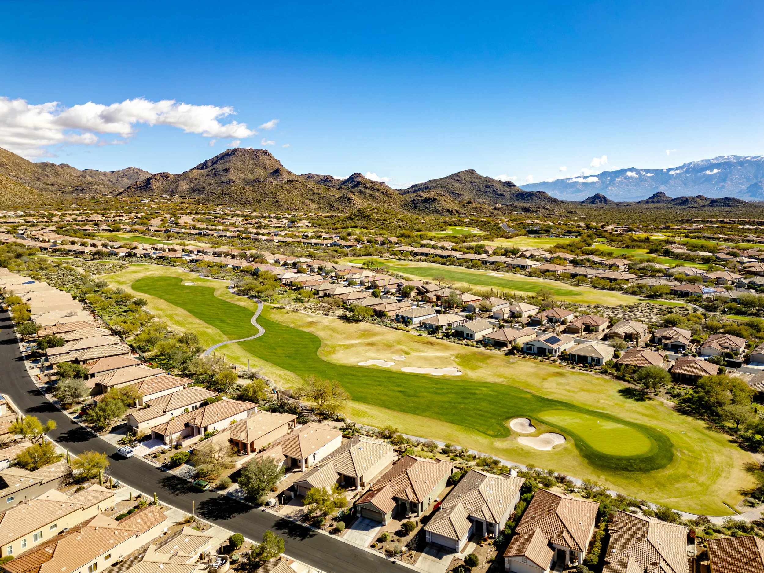 Drone photo overlooking the Dove Mountain community in Marana, Arizona, with golf course greens, desert homes, and rugged mountain landscapes under a bright blue sky.