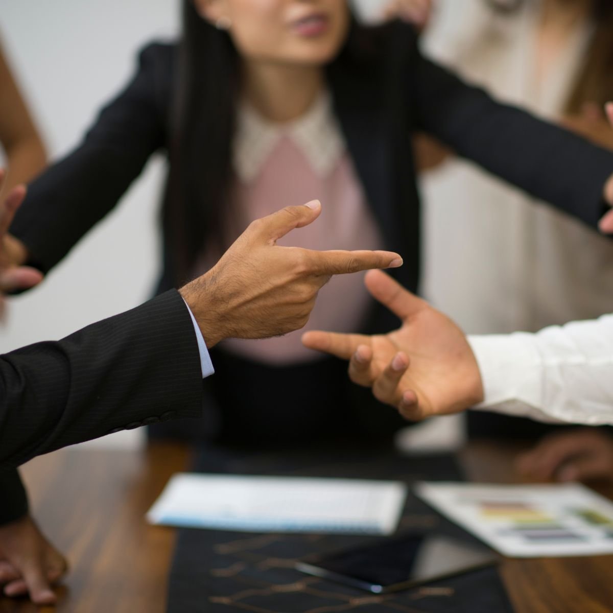 People arguing around a table, with one person pointing a finger at another.