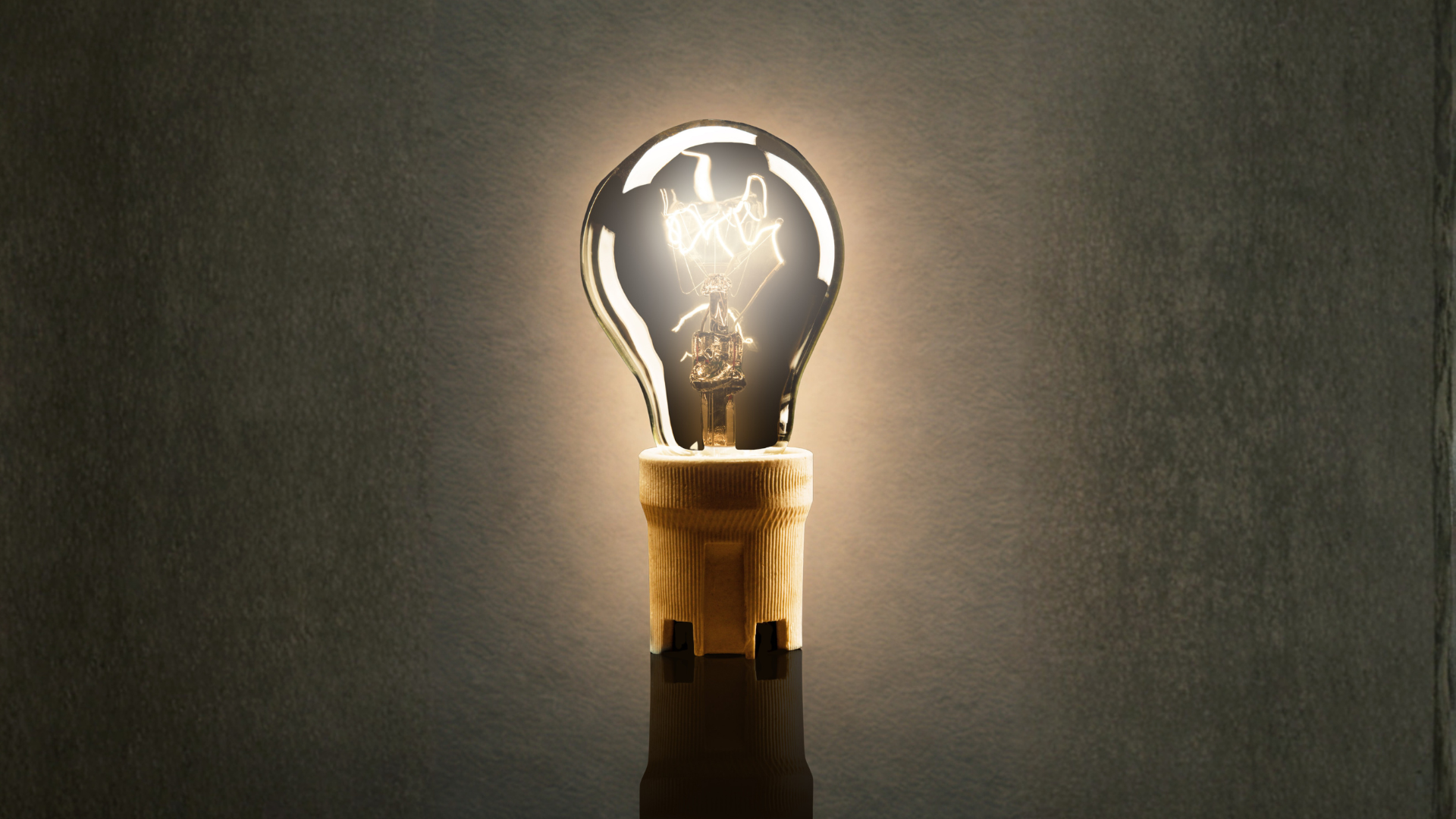A close-up photo of an illuminated incandescent light bulb with a glowing filament against a dark background.