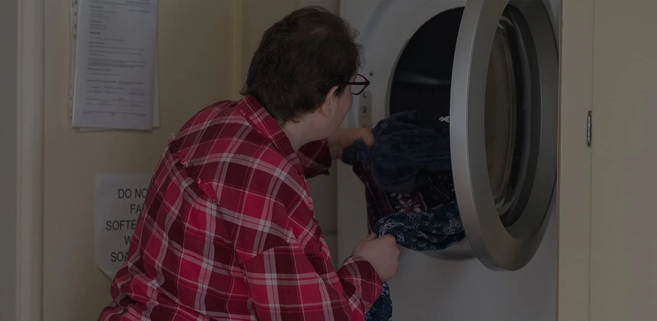 Woman in plaid shirt pulling laundry out of the washing machine.