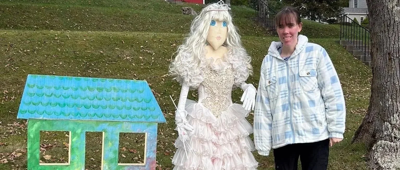 A woman standing next to a princess scarecrow