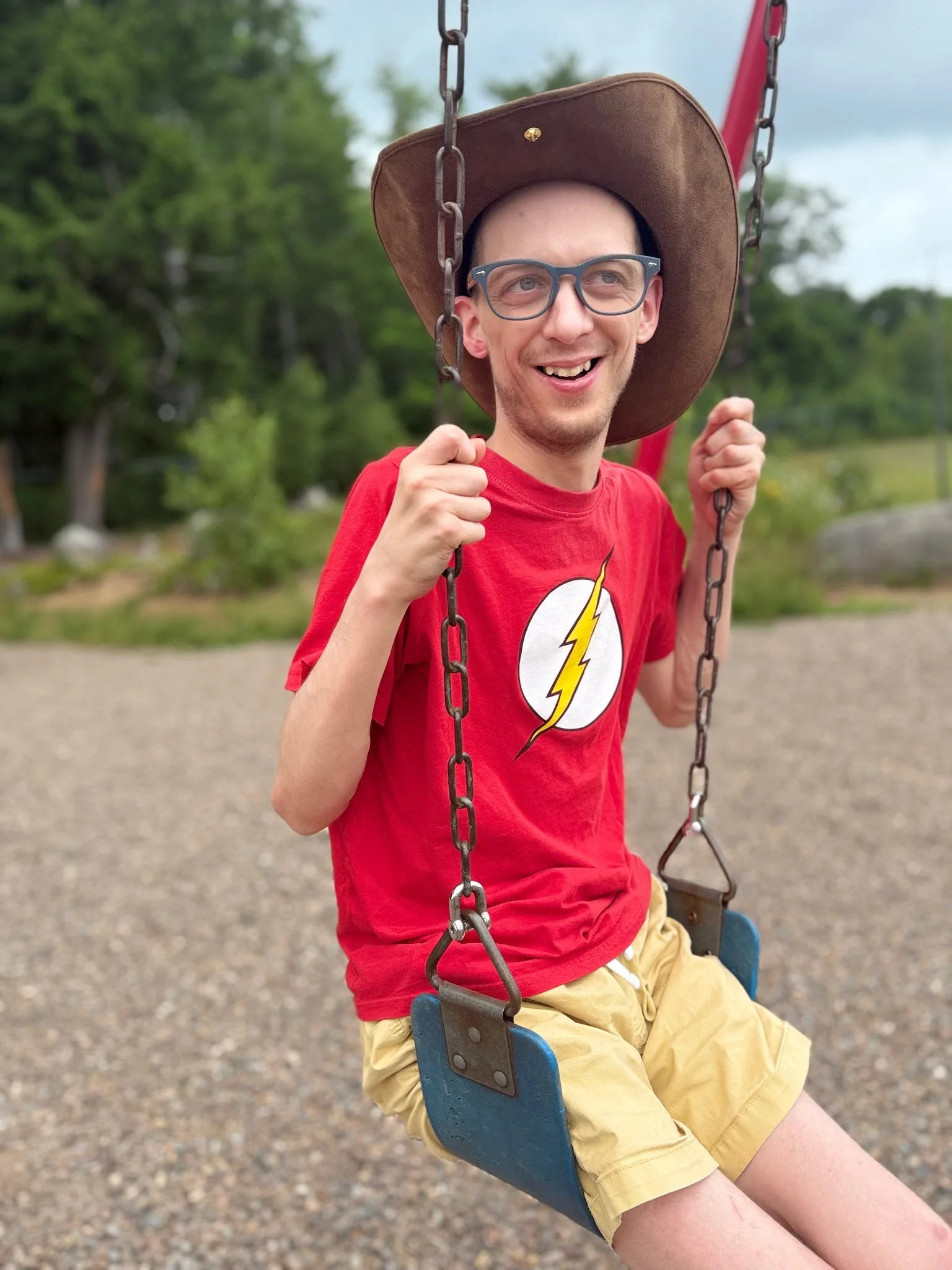 Young man sitting on swing, smiling, wearing a cowboy hat.