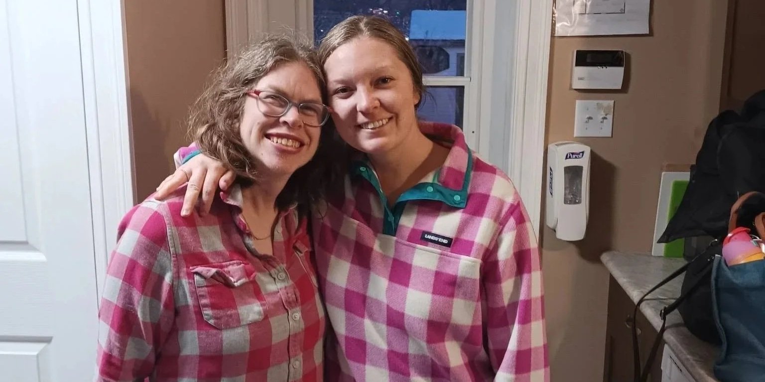 Two women standing beside each other, both wearing plaid shirts