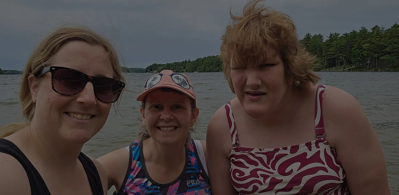 Three women smiling for the camera with water in the background.