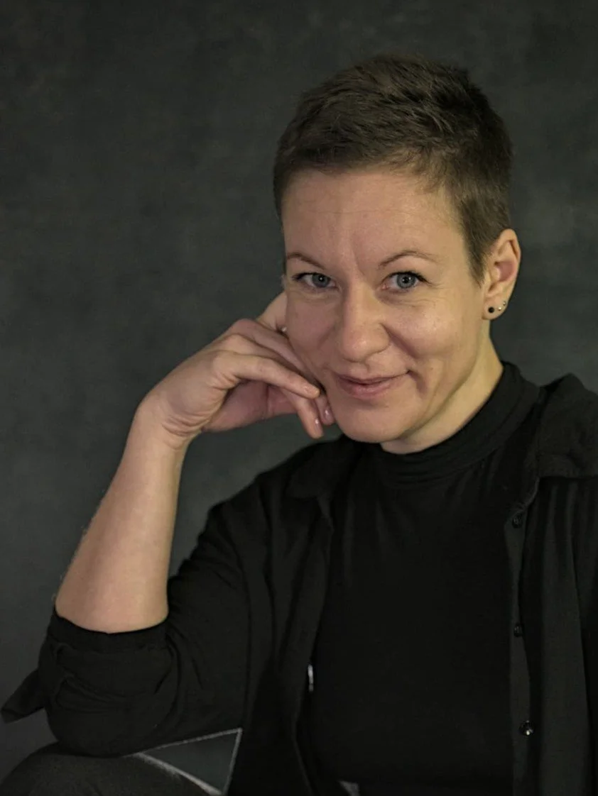 Sexual- und Beziehungscoach Eva Hanson lächelnd im schwarzen Hemd, eine Hand an ihrer Wange