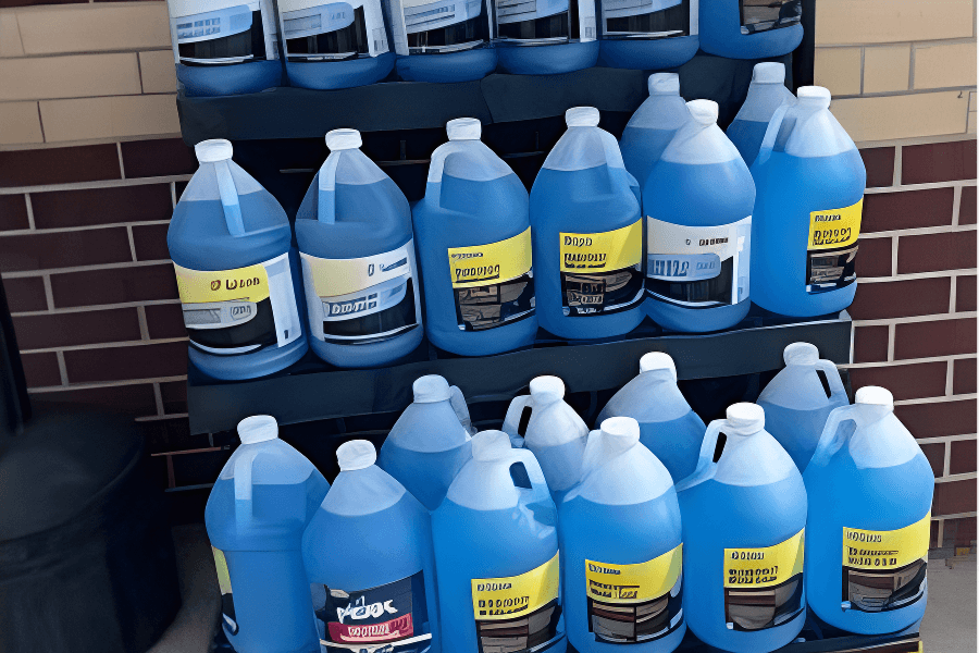 A display shelf with multiple large bottles of blue liquid cleaning solutions arranged in two rows in front of a brick wall.