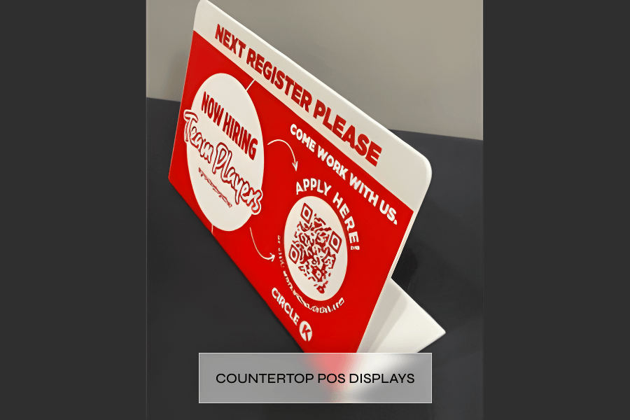 Red and white tabletop sign advertising new job openings, encouraging people to apply via a QR code, with a circular logo for 'Team Players' and instructions to come work with them.