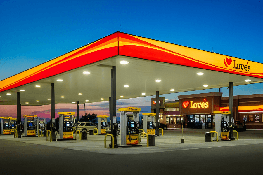 A Love's gas station at dusk with multiple fuel pumps, a convenience store, and a colorful sky in the background.