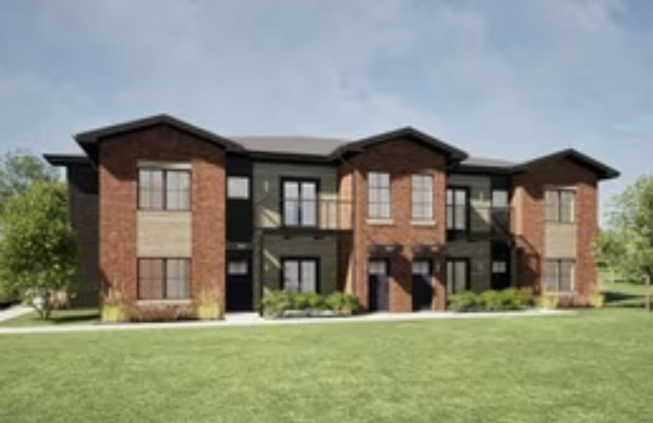 A three-story residential apartment building with brick and stone exterior, multiple windows, and a landscaped lawn in front.
