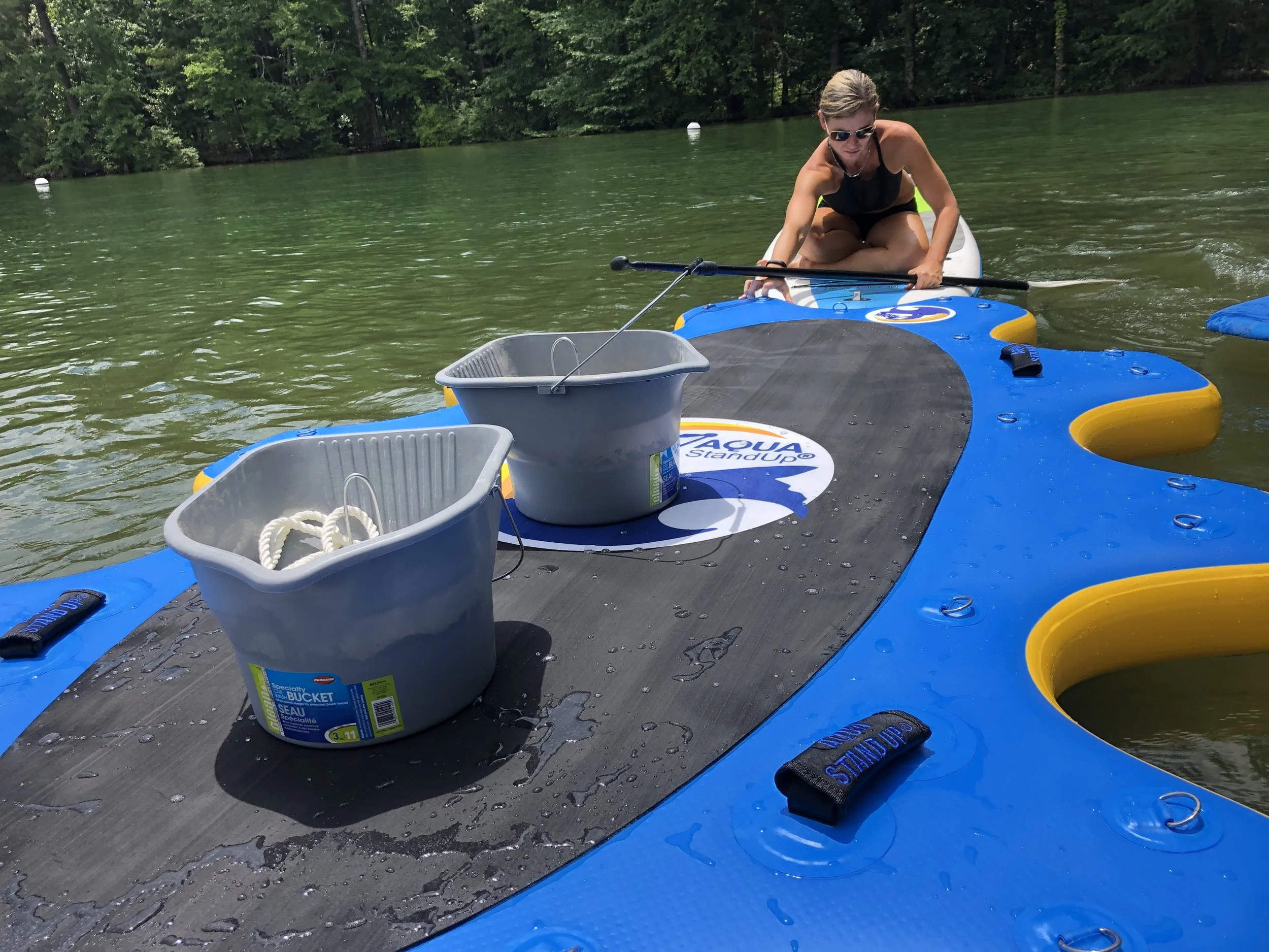 aquastandup platform set up on a lake with some buckets to maintain it in a spot with someone assisting in setting up everything