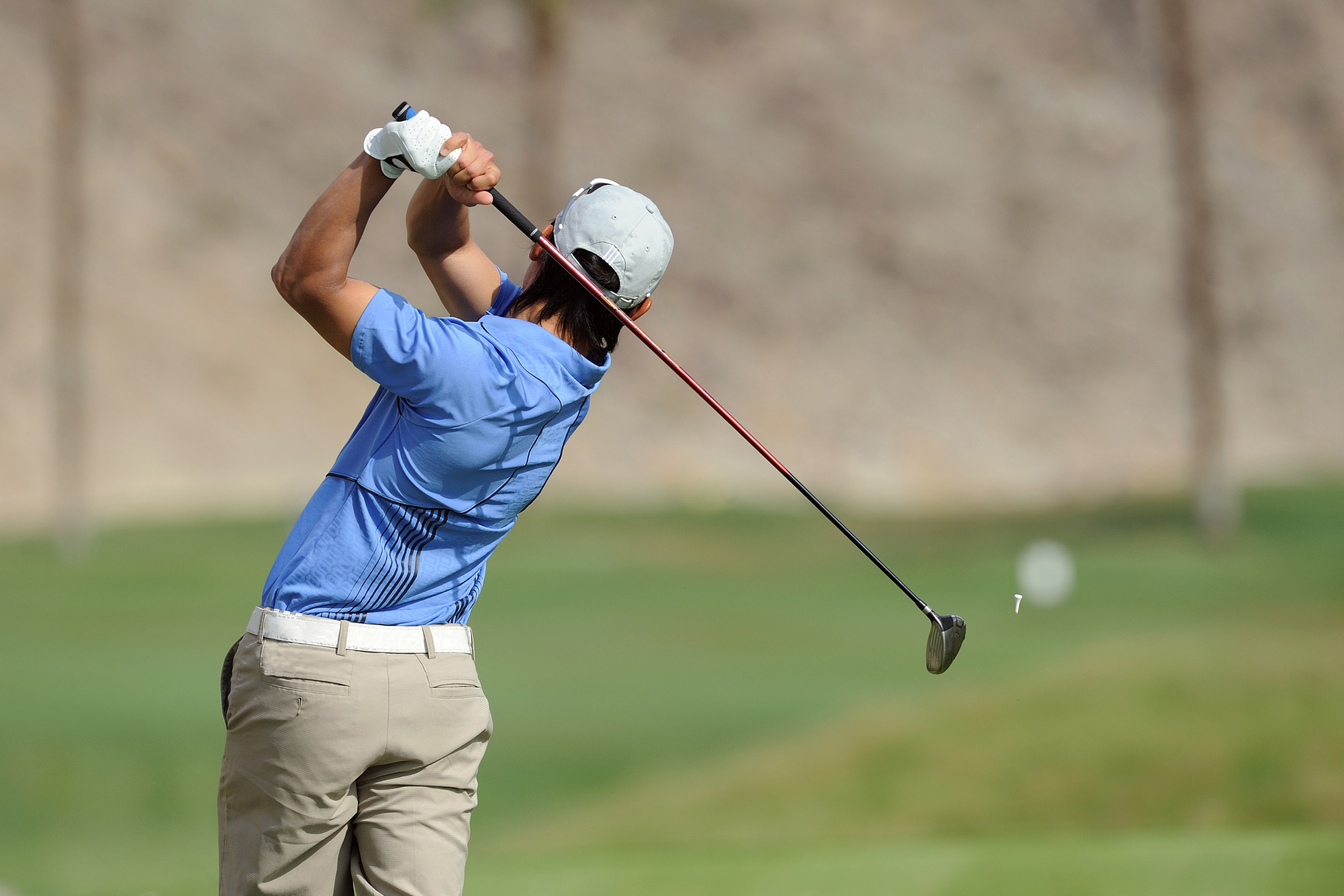 A golfer professional during a swing with blue shirt and beige trousers holding a club