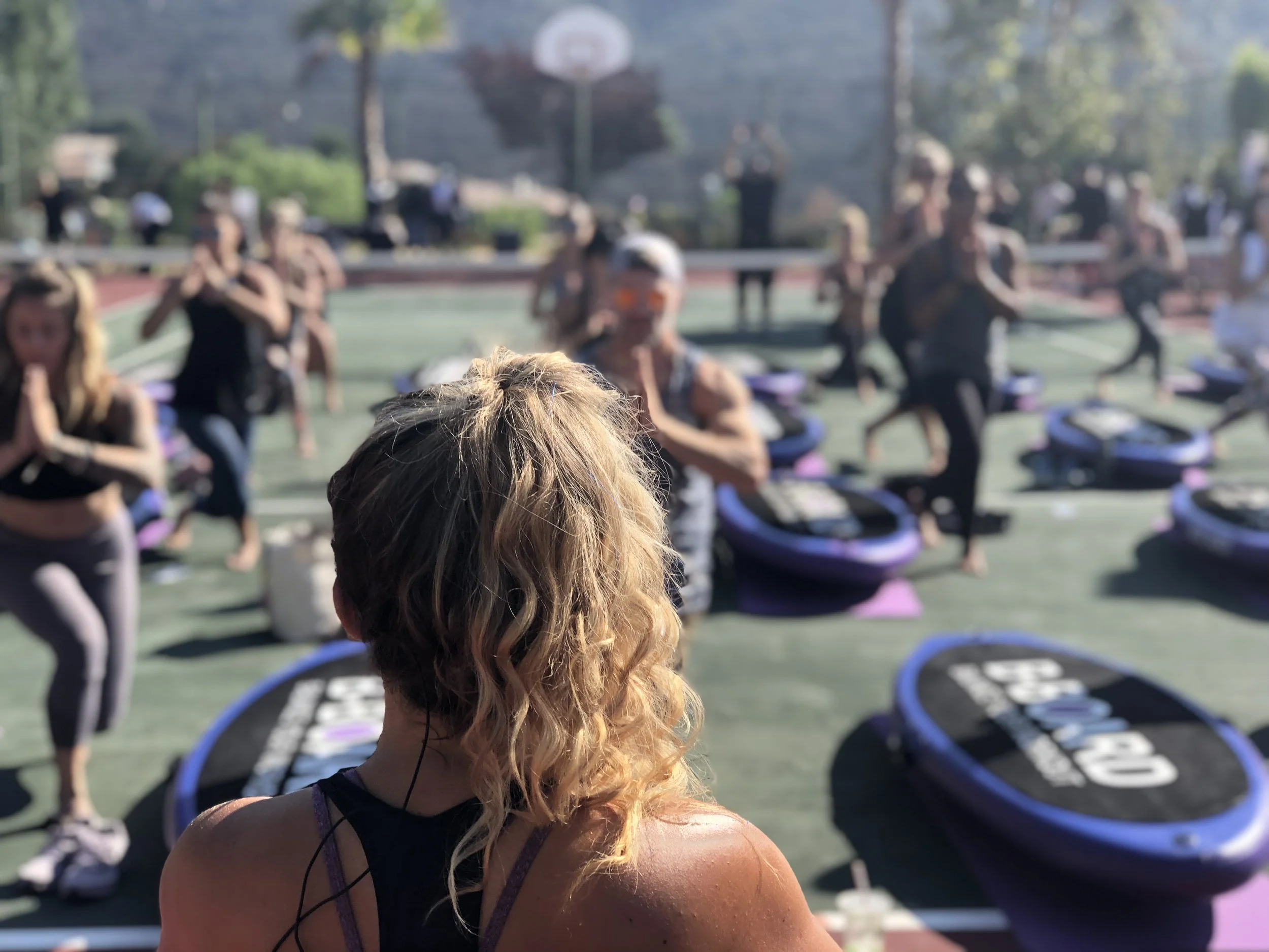 triner in front of participants during a B-BOARD® class on a tennis court with palm trees in the background