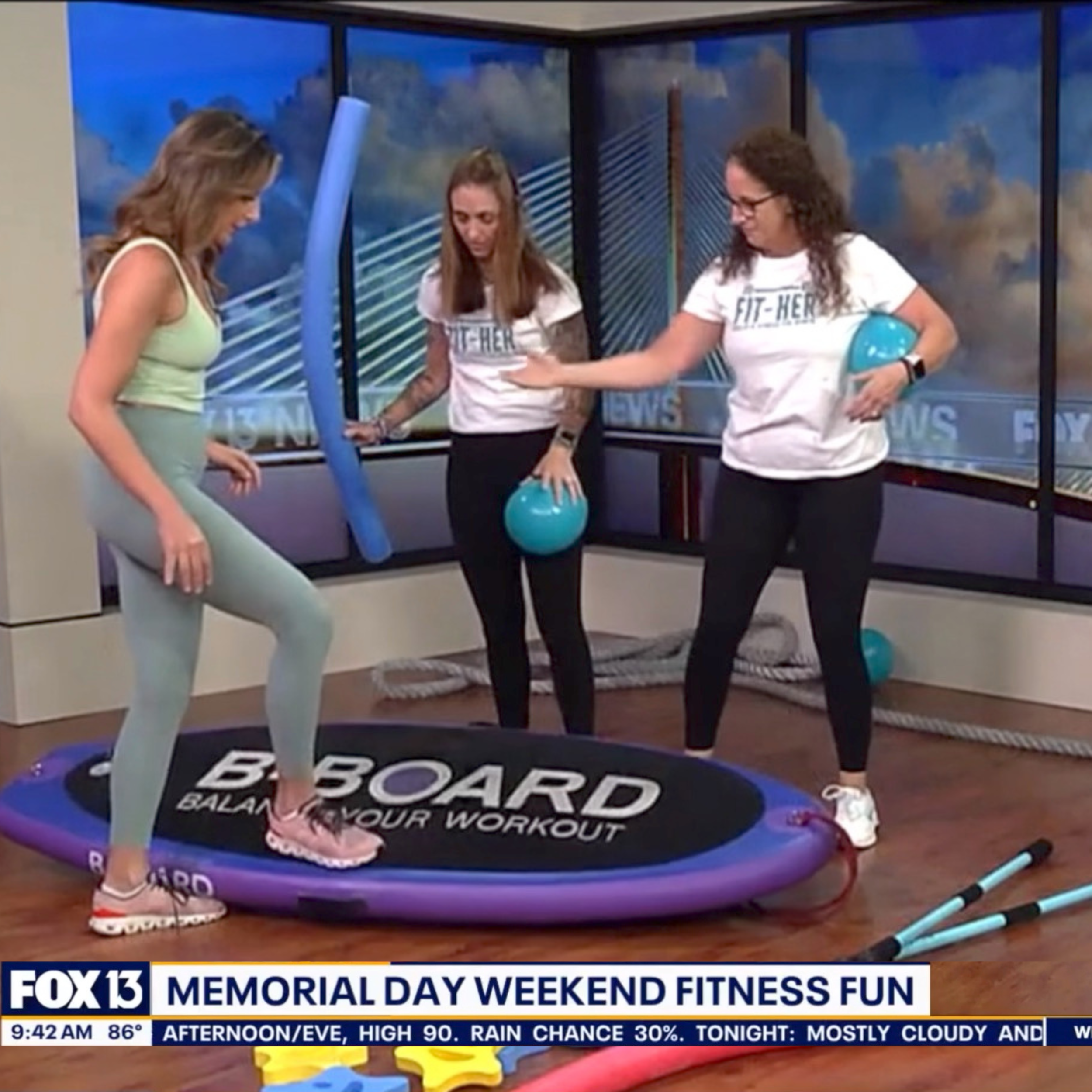 Anchor of Good Day Tampa Fox 13 getting on the B-BOARD with 2 coaches from Fit Her  with Ann Gilbert, title on screen Memorial Day Weekend Fitness Fun