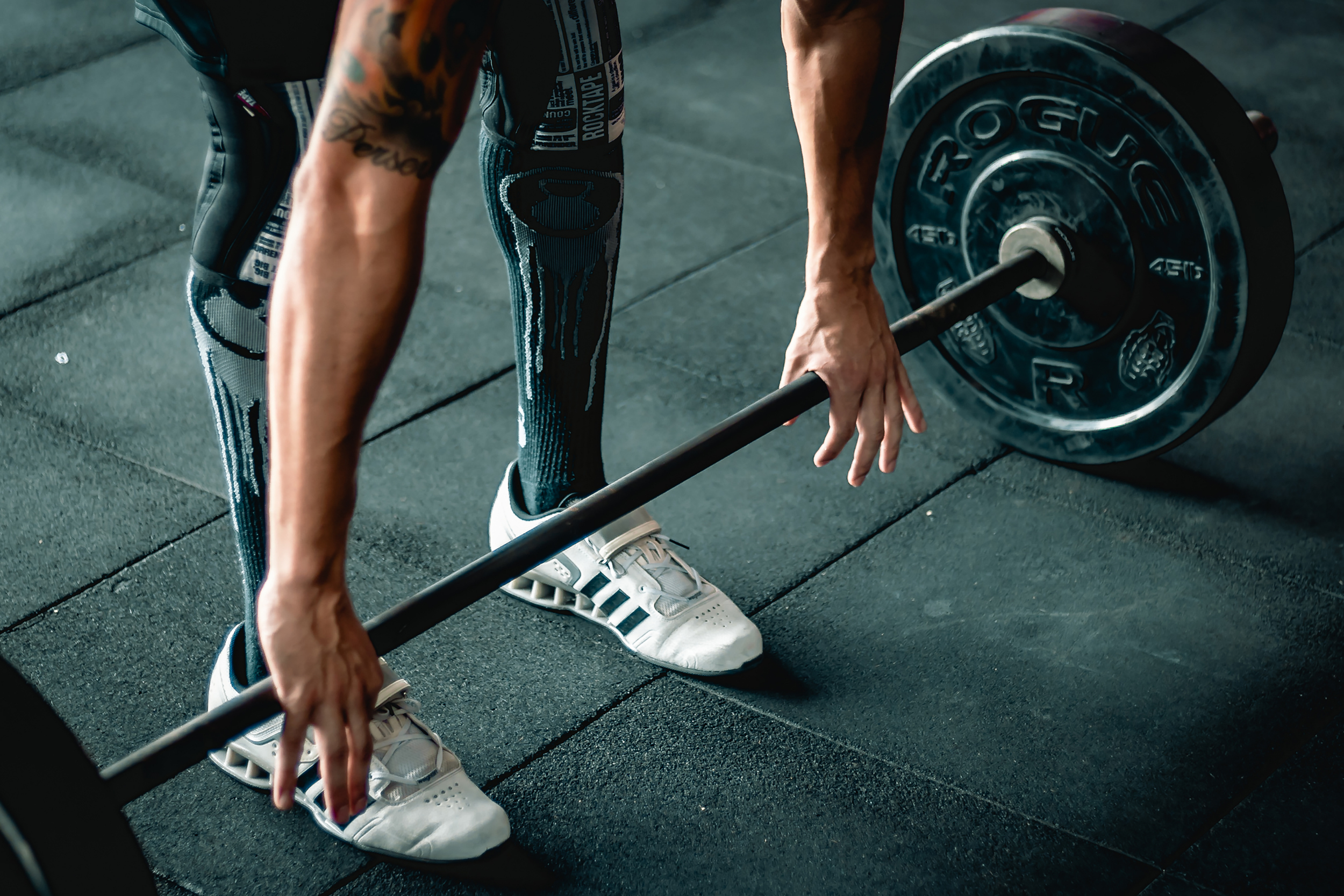 person wearing weightlifting shoes ready to lift a barbell with heavy weight on it in a gym setting