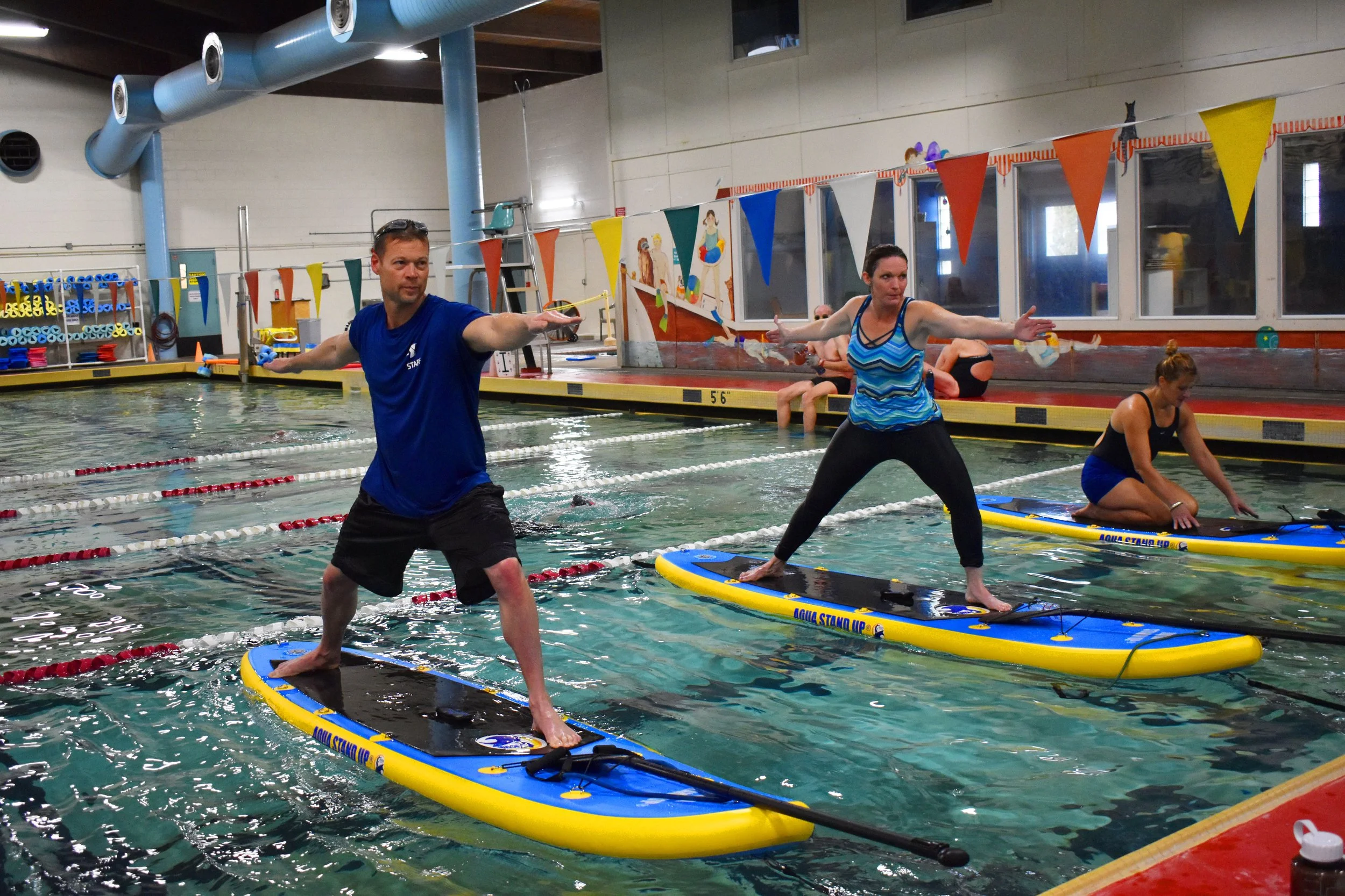 a group of participants performing warrior 2 on paddle boards in a swimming pool