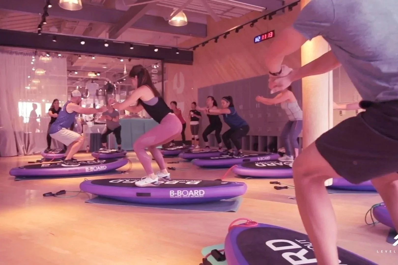 People participating in a group indoor fitness class on balance b oards, practicing balance and squats on purple B-Board balance boards in a gym studio.