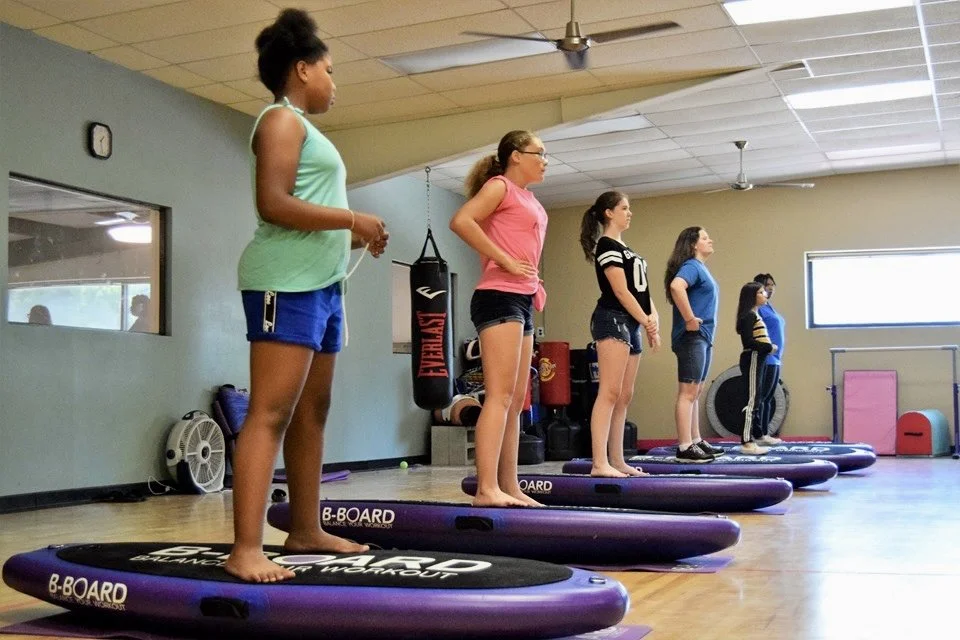 Five young girls in workout attire standing on balance board B-BOARD®  in a fitness studio, preparing for a kid class.