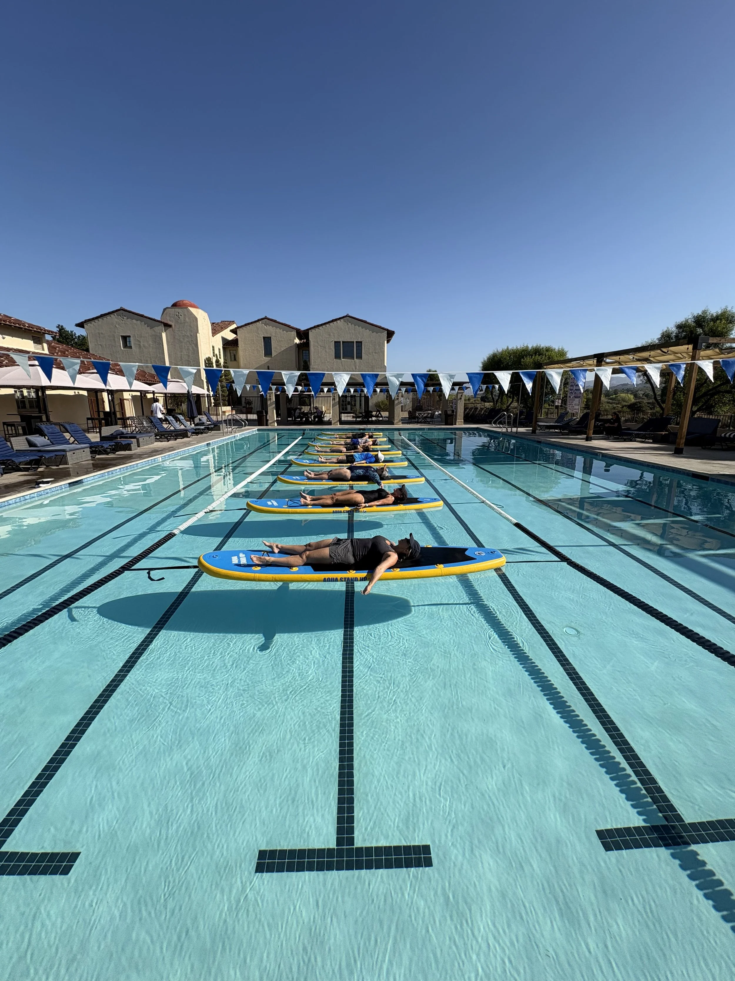 participants lying down for a meditation on the boards and relaxing after an aquastandup session in a swimming pool pristine water blue sky