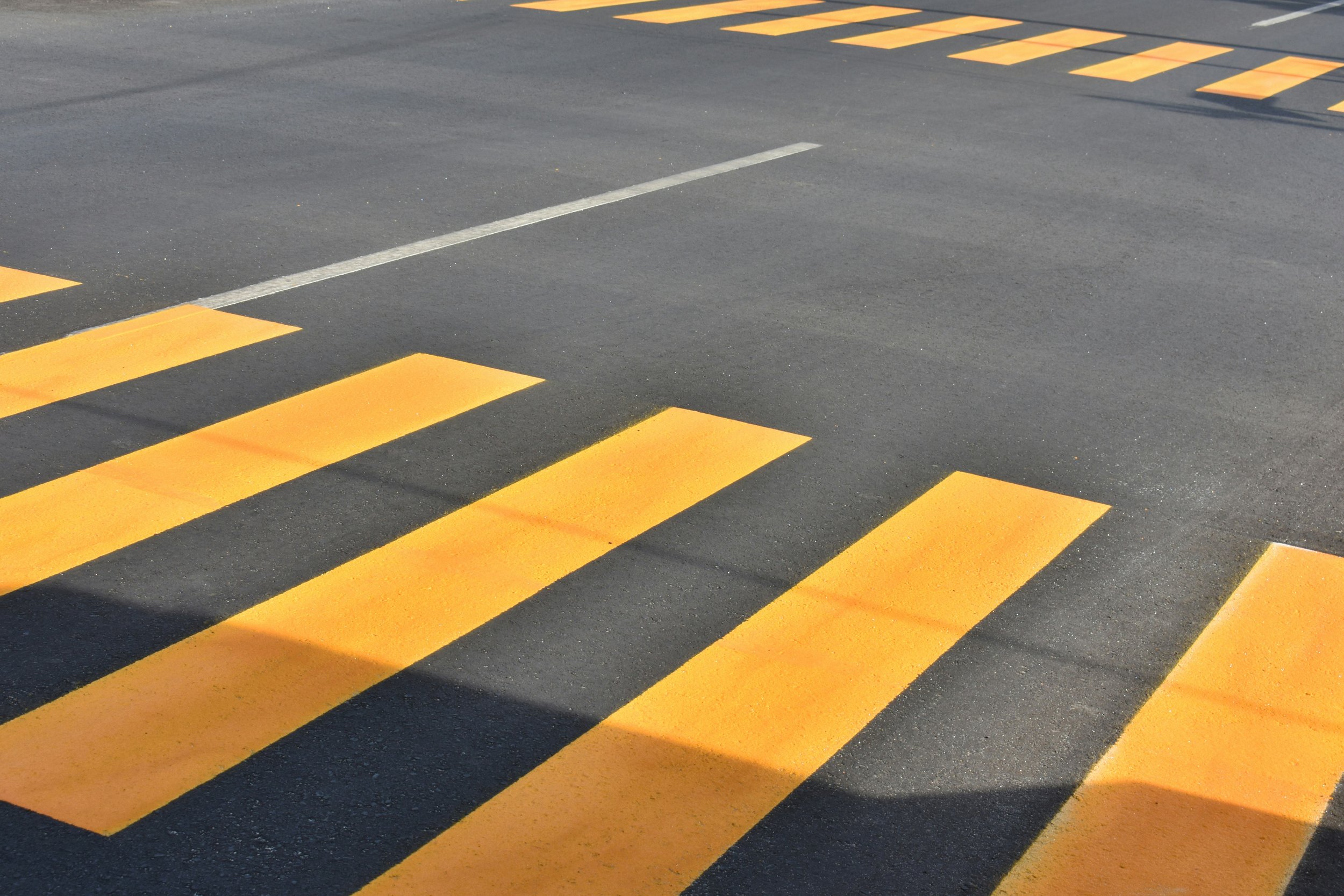 Yellow striped thermoplastic pedestrian crosswalk on asphalt road.