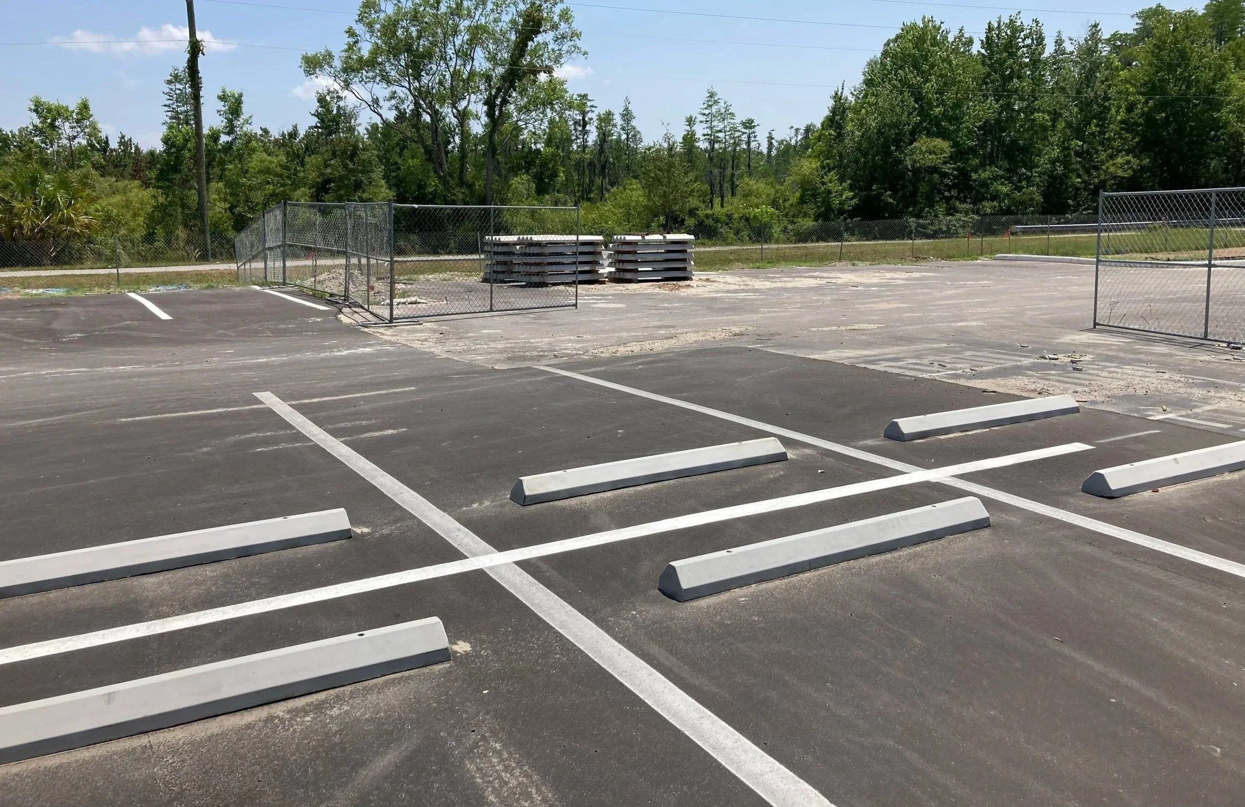 Empty parking lot with some debris, fenced-off section, and trees in the background.