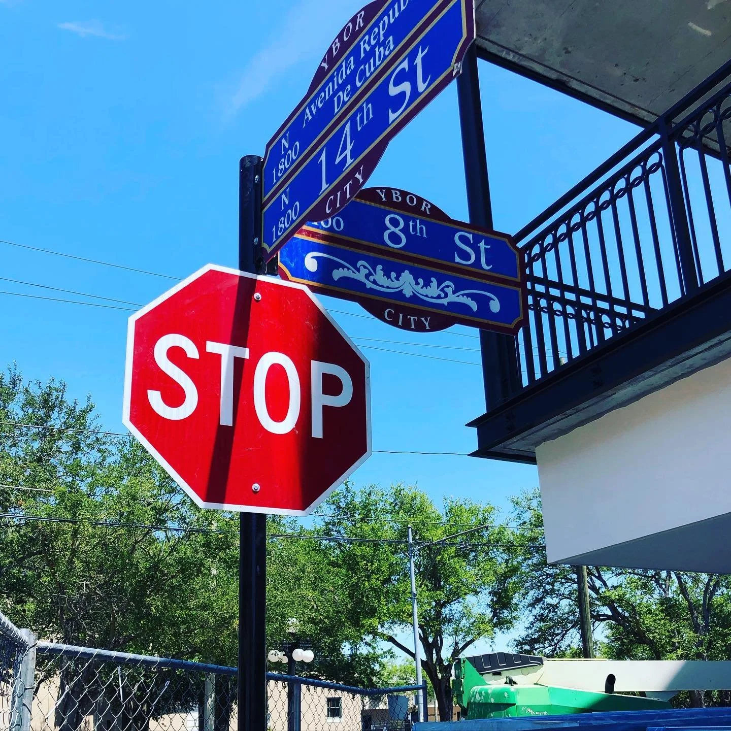 Street sign at the intersection of 14th Street and 8th Street in Ybor City, Tampa, Florida, with a red stop sign in the foreground and green trees in the background.