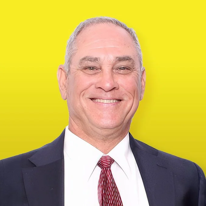 Photo of Jon Martin, founder of Universal Pavement Marking, smiling and wearing a dark suit against a bright yellow background.