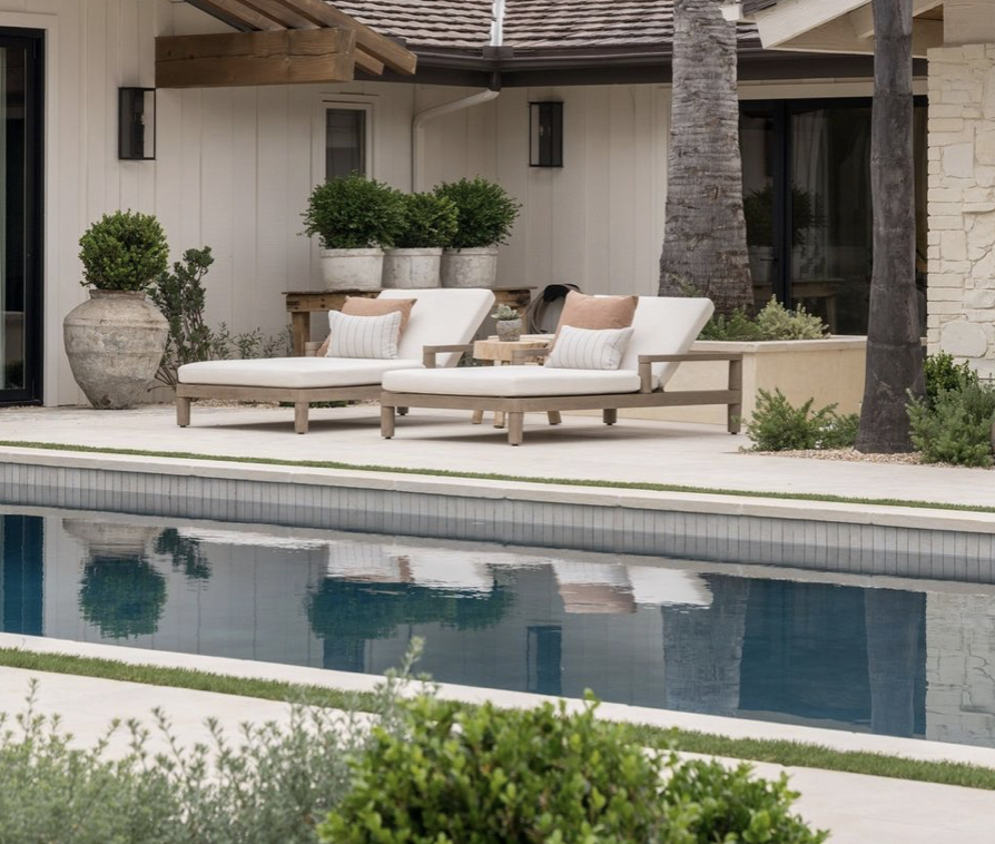 Residential backyard with swimming pool, two white lounge chairs with beige pillows and striped cushions, potted plants, and trees.