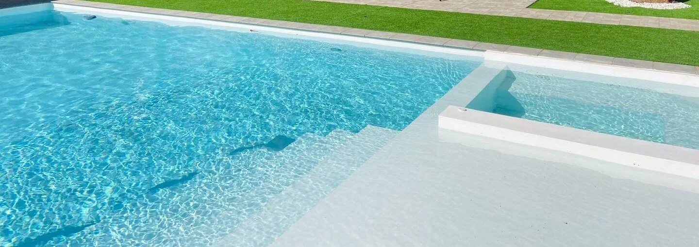 Empty swimming pool with blue water, white pool edges, grassy area in the background.