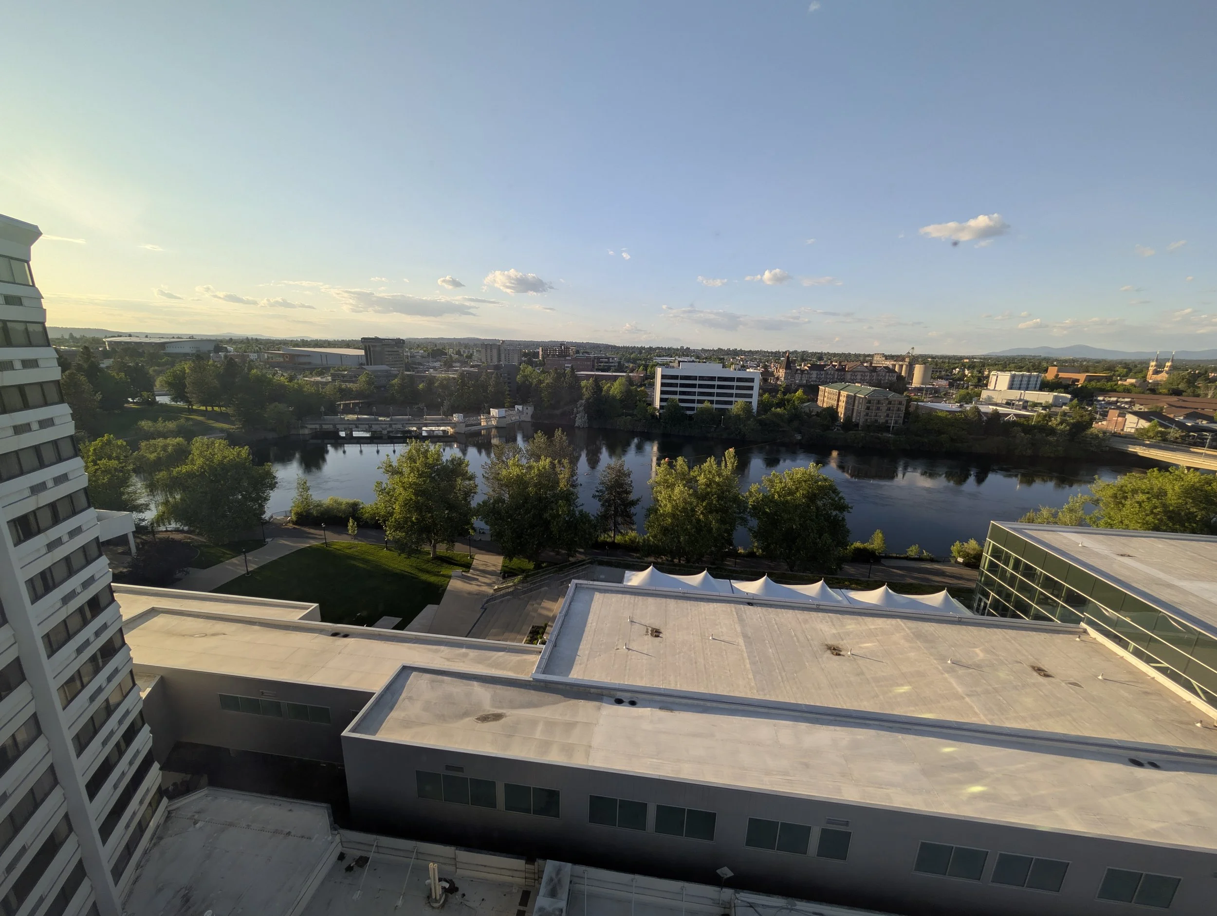 A cityscape view from a high-rise building showing a river, green trees, and various buildings under a blue sky with some clouds.