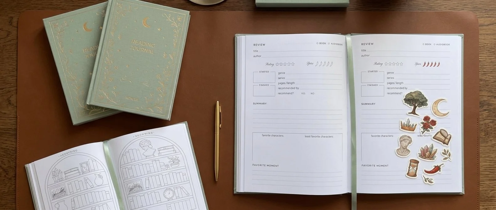 Open journals with book review templates, stickers, and a gold pen on a wooden desk.