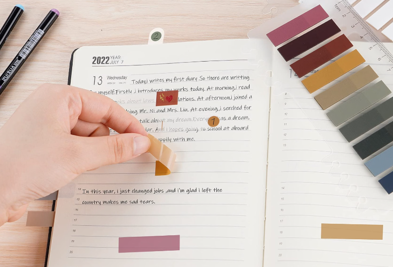 Open planner with handwritten notes, colorful sticky tabs, and markers on a wooden desk.