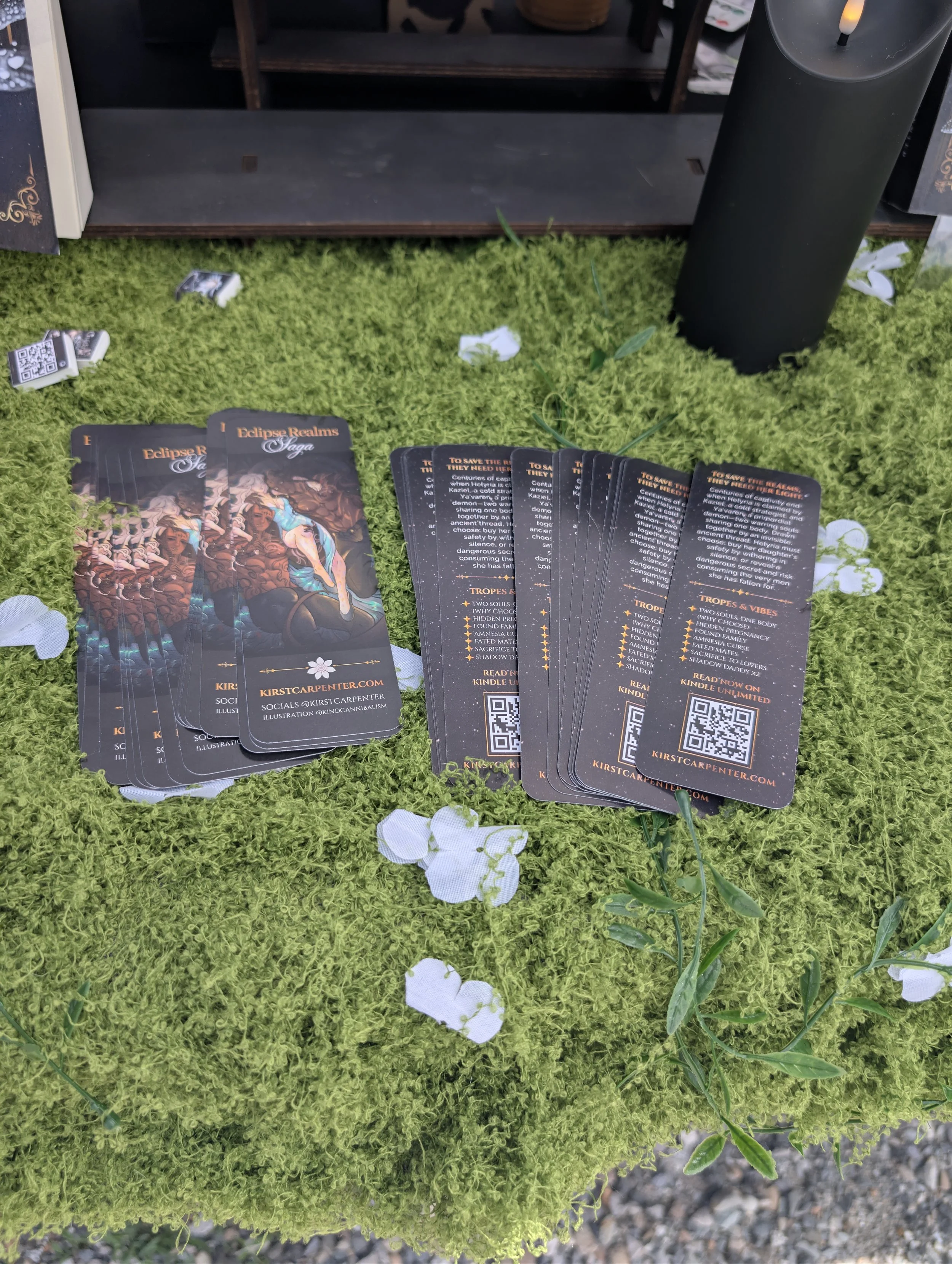 Fanned out tarot cards on green grass, with a black candle and some small white cloth pieces around.