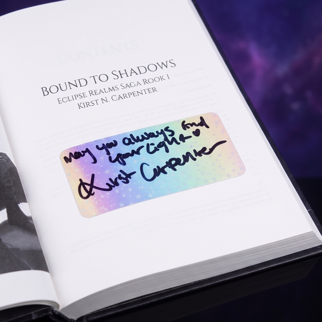 Open book showing the title 'Bound to Shadows' by Kirst N. Carpenter, with a handwritten note on a rainbow-colored sticker that reads 'May you always find your way back. ♥ Kirst Carpenter'.