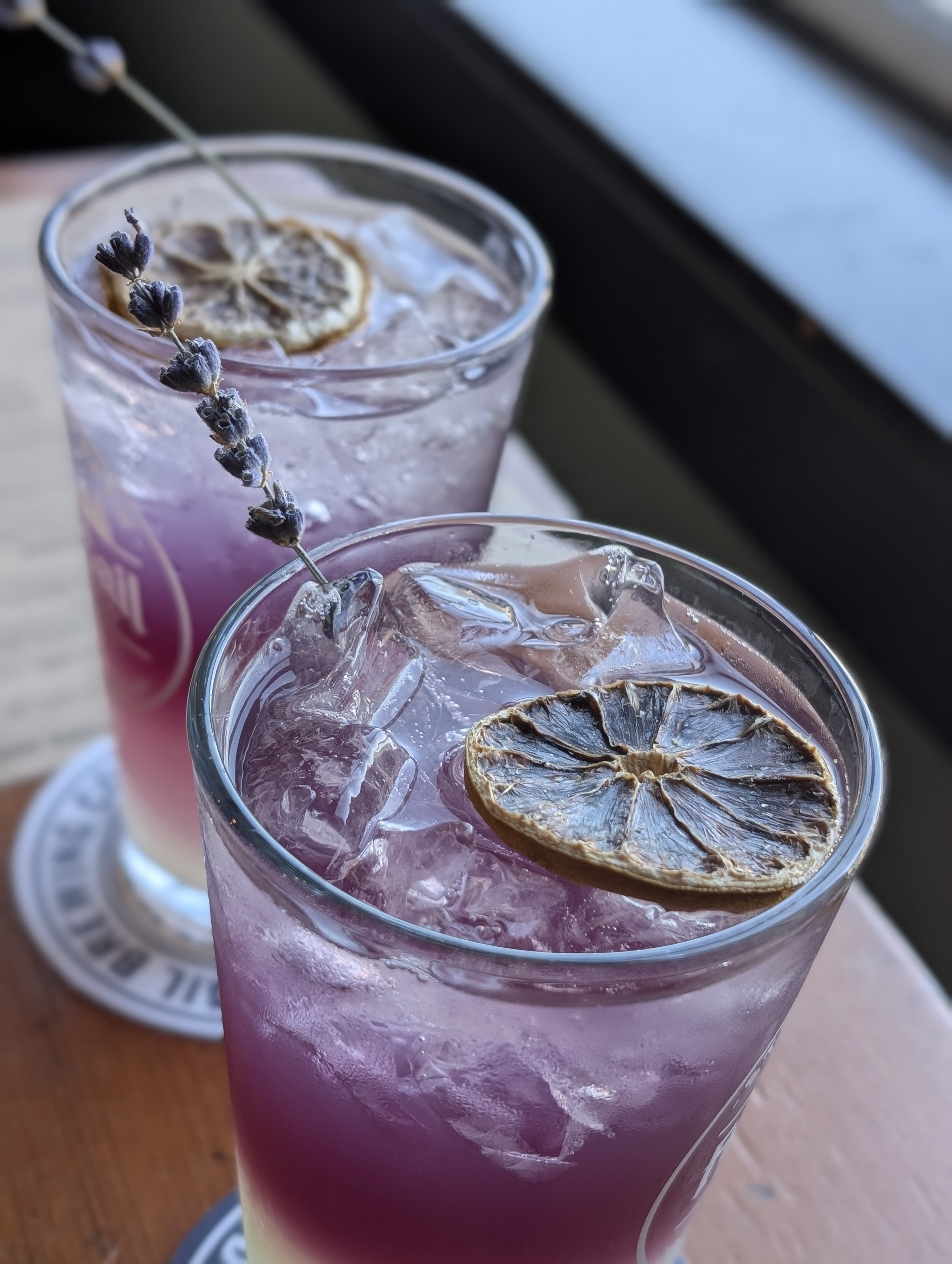 Two glasses of lavender-colored beverage with ice, garnished with dried lemon slices and lavender sprigs.