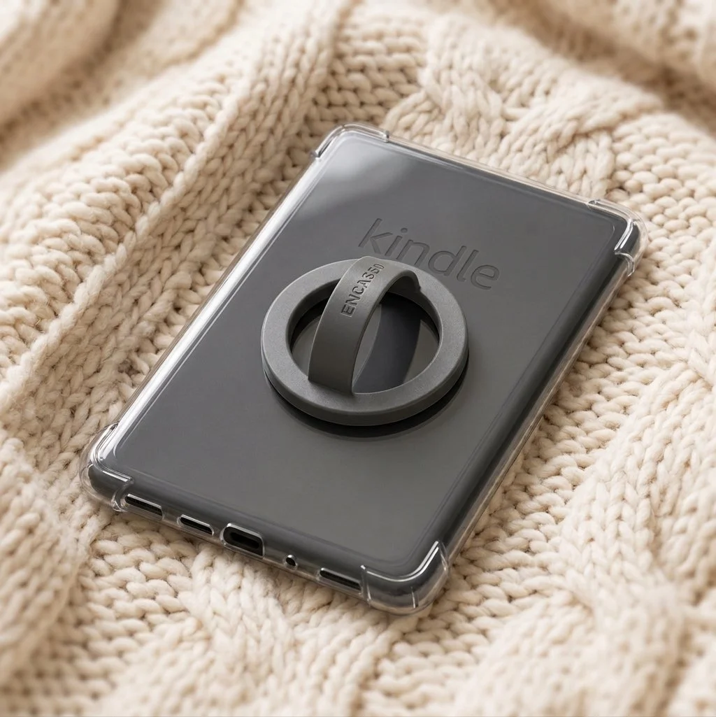 A Kindle e-reader with a grey tablet case and a ring-shaped holder, resting on a soft beige knitted blanket.