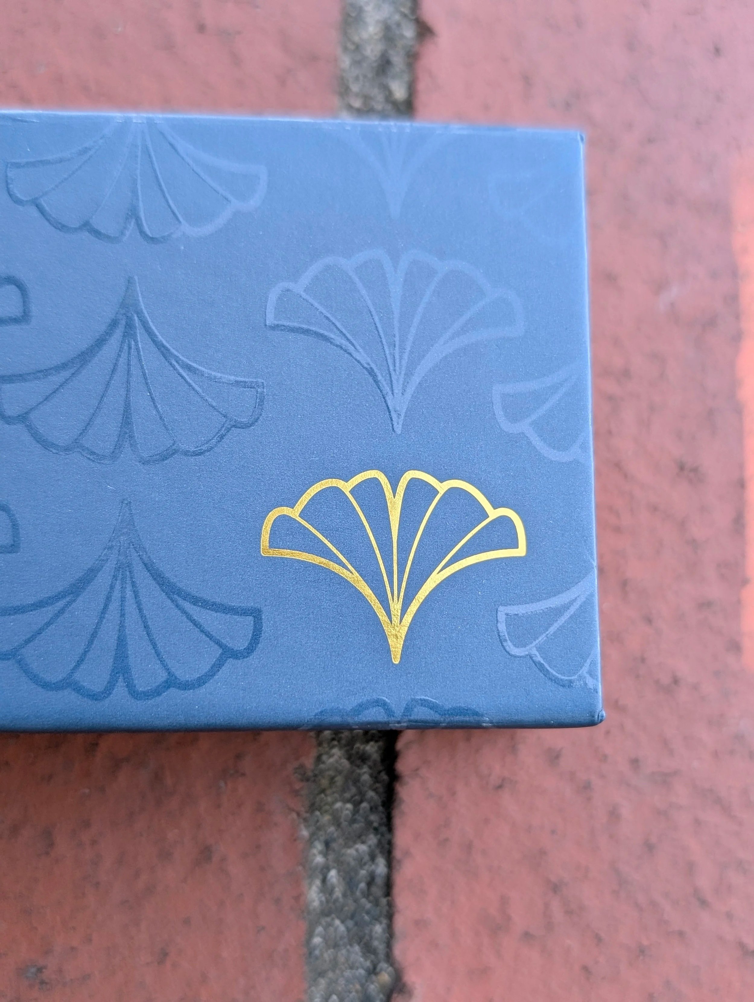 Close-up of a blue box with floral patterns and a gold design on a pink and gray tiled surface.