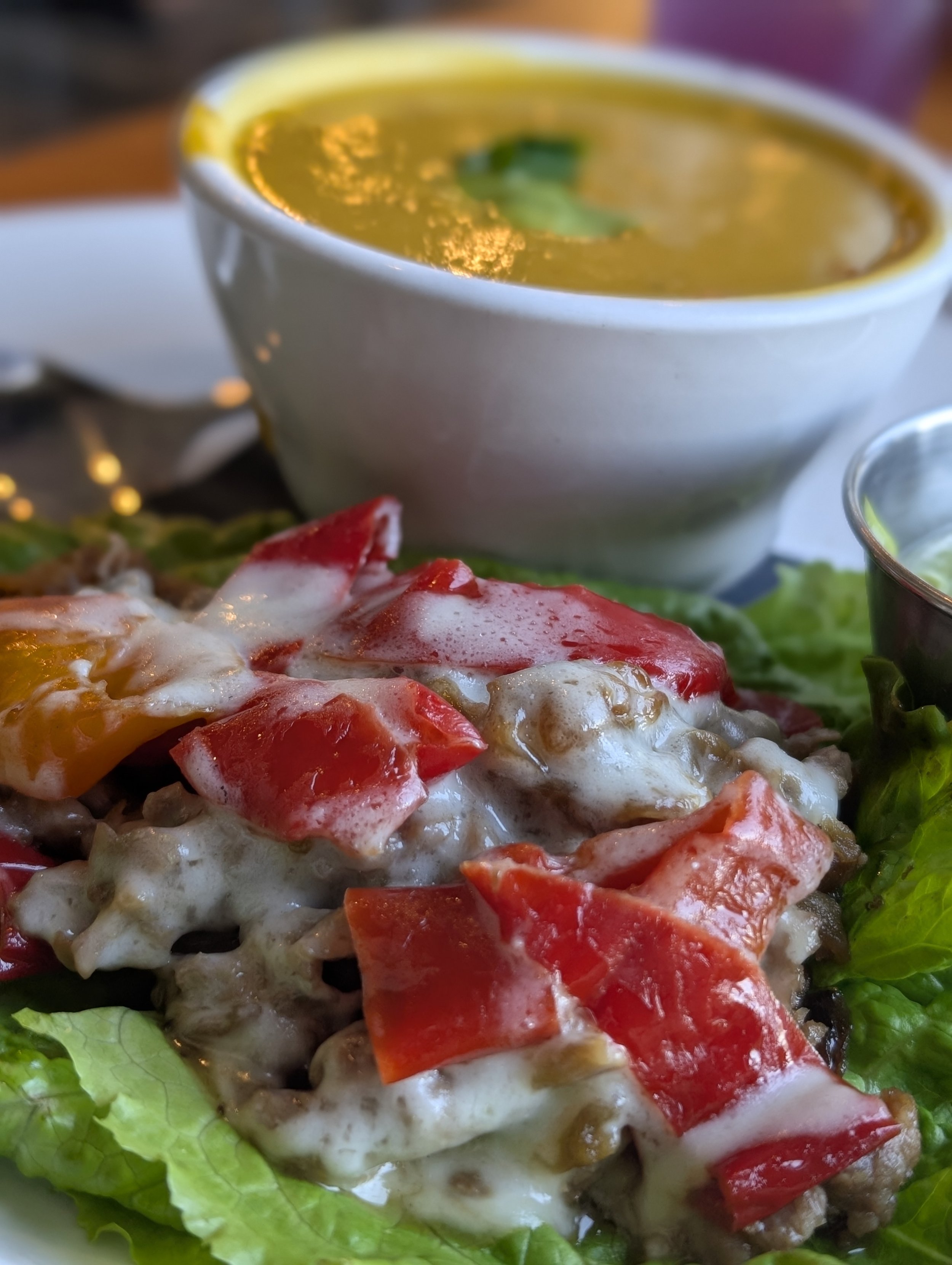 A white bowl of yellow soup with green garnish, placed next to a salad with greens and cherry tomatoes.