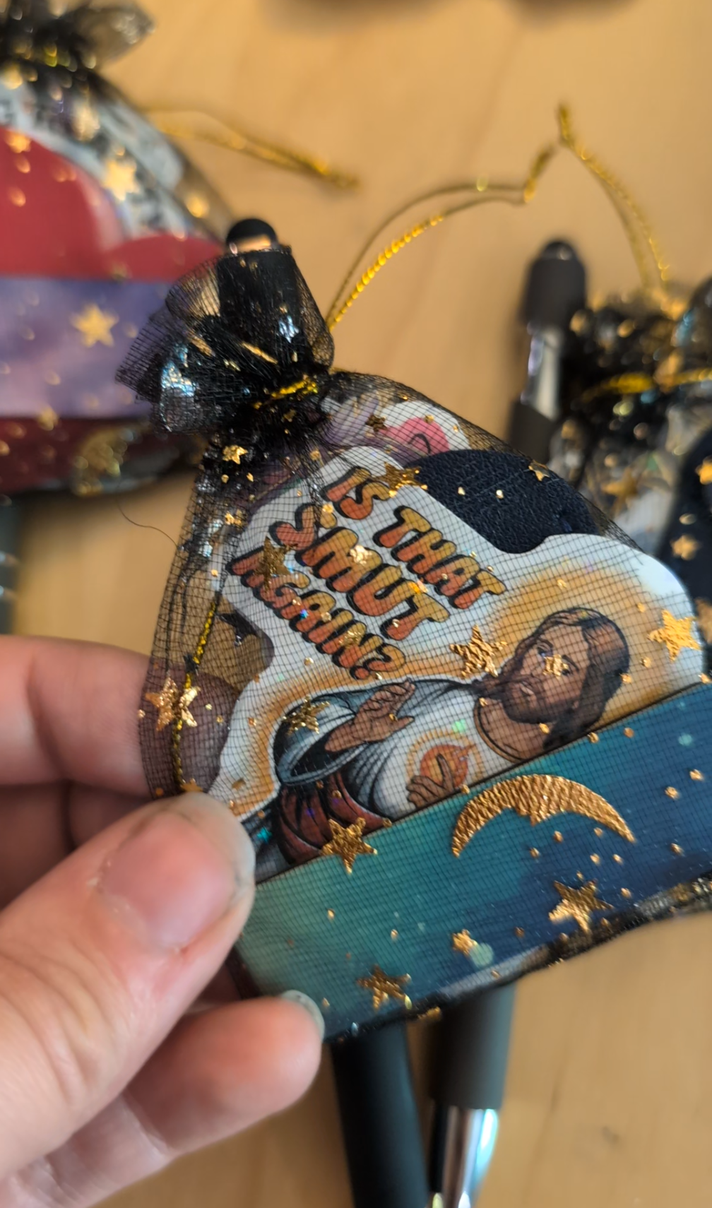 A mesh bag with a cartoon graphic of a man holding a slice of pizza, decorated with gold stars and moons, is held by a person's hand. The bag appears to have a tag that reads 'THAT'S MY PIZZA!'