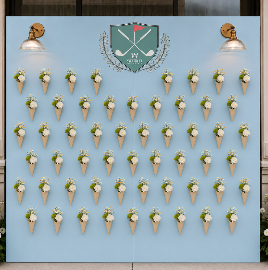 A decorative display on a light blue wall with small cone-shaped posey bouquets arranged in a grid. Each posey contains white flowers and green foliage. There are two mounted lamps and an emblem at the top center that features crossed golf clubs.