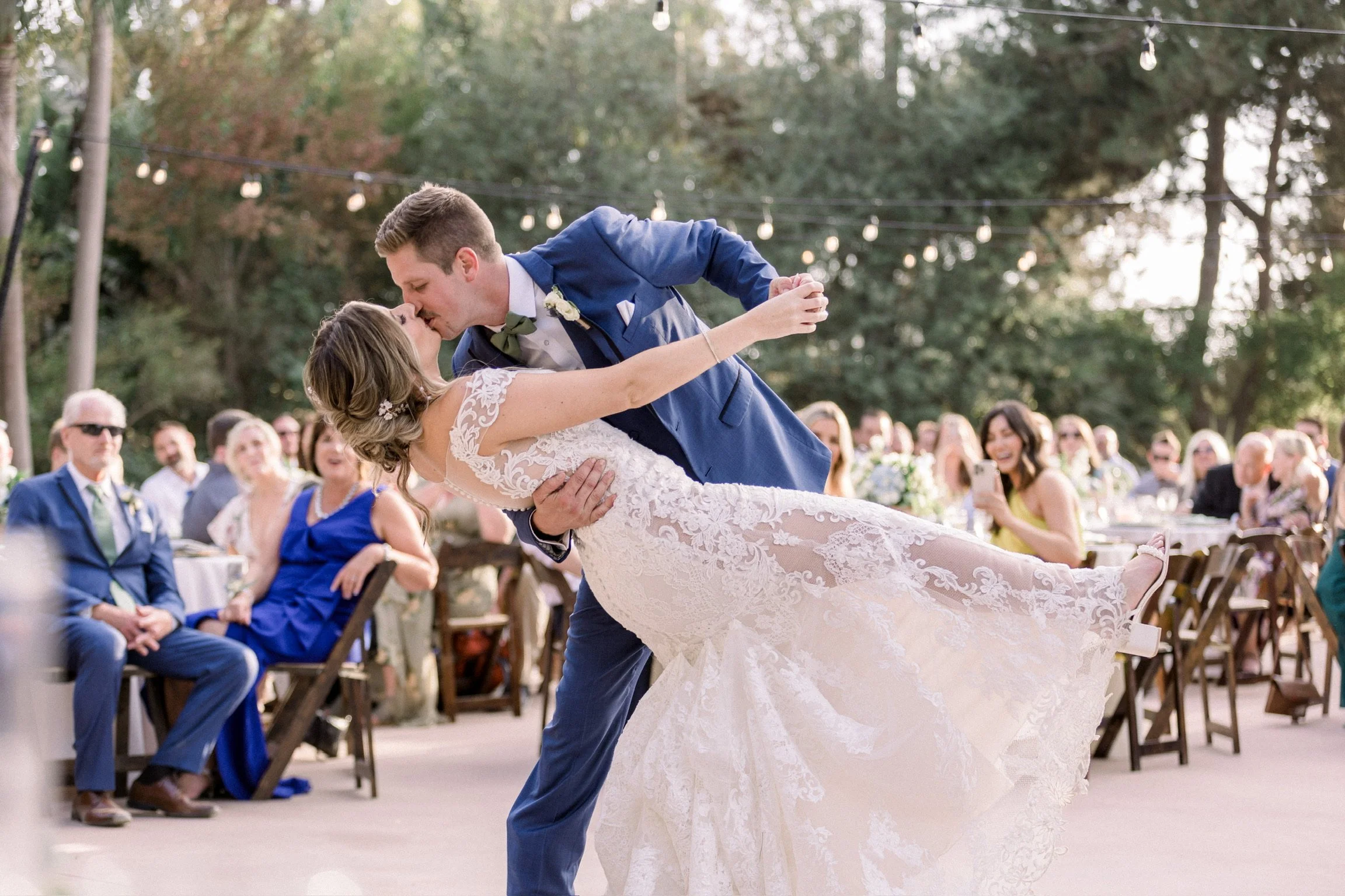 A bride and groom sharing a dance at their wedding reception outdoors, with guests watching and taking photos.
