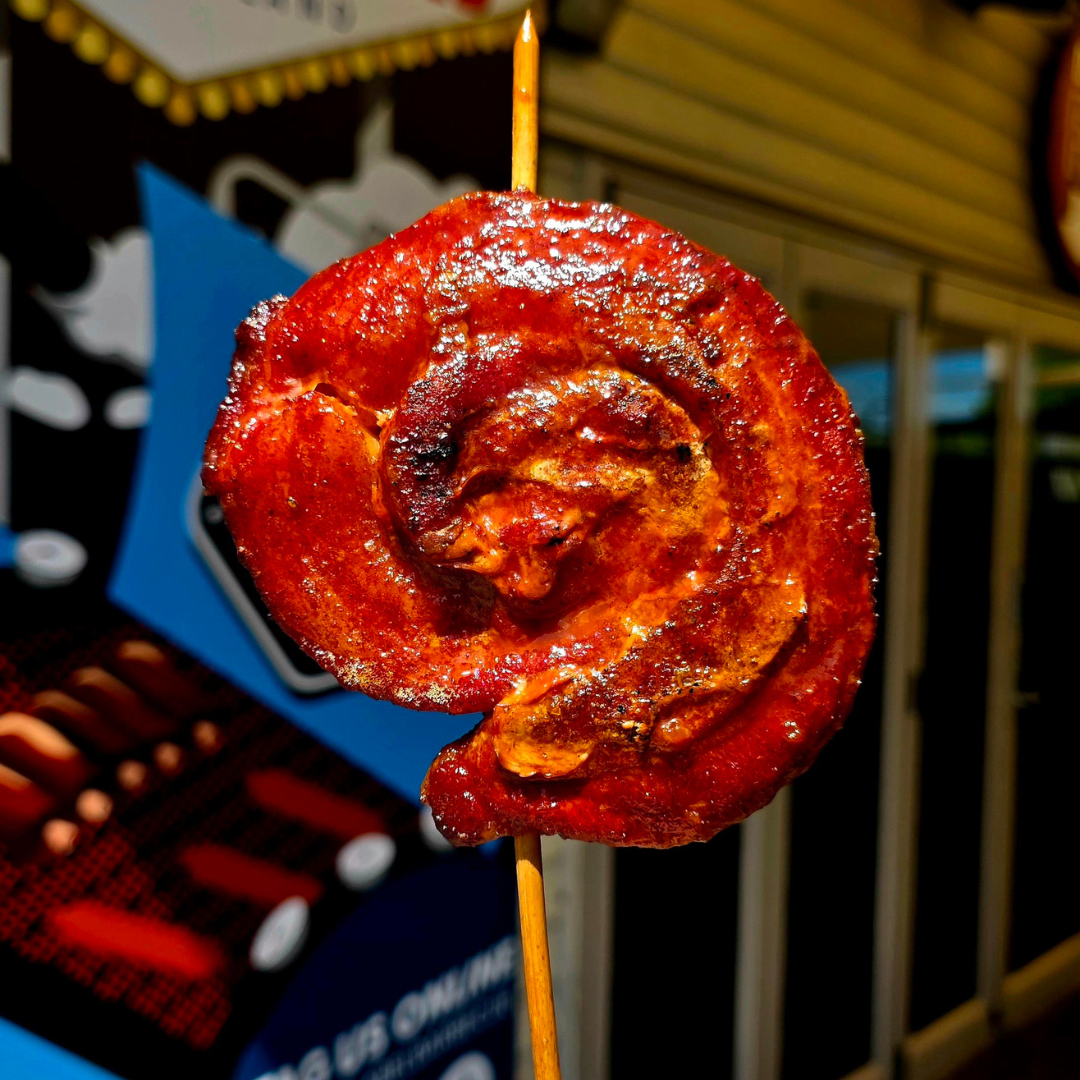 Close-up of a cooked, glazed sausage spiraled on a skewer, with a caramelized surface.