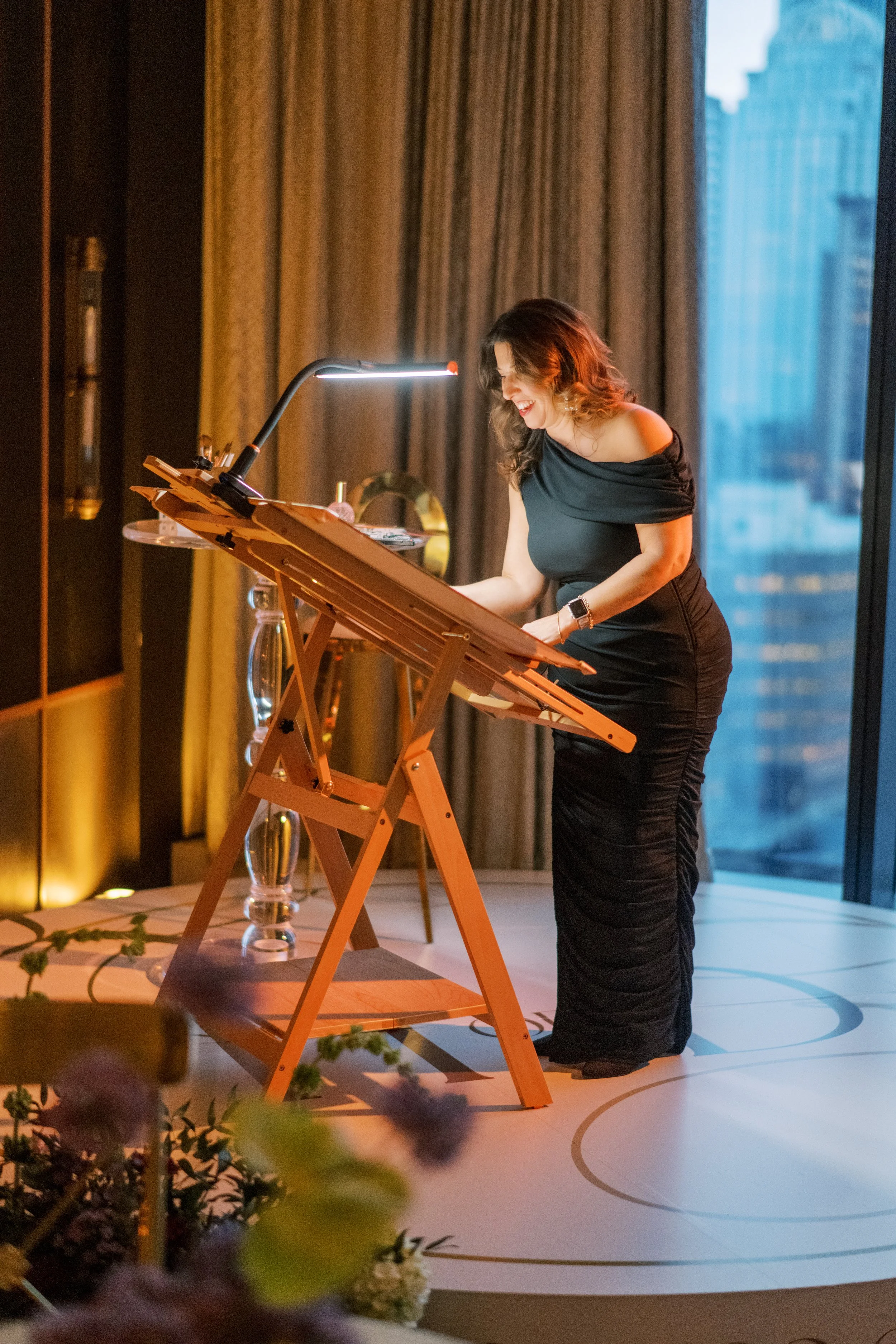 Artist on a platform smiles as she paints for a luxury wedding